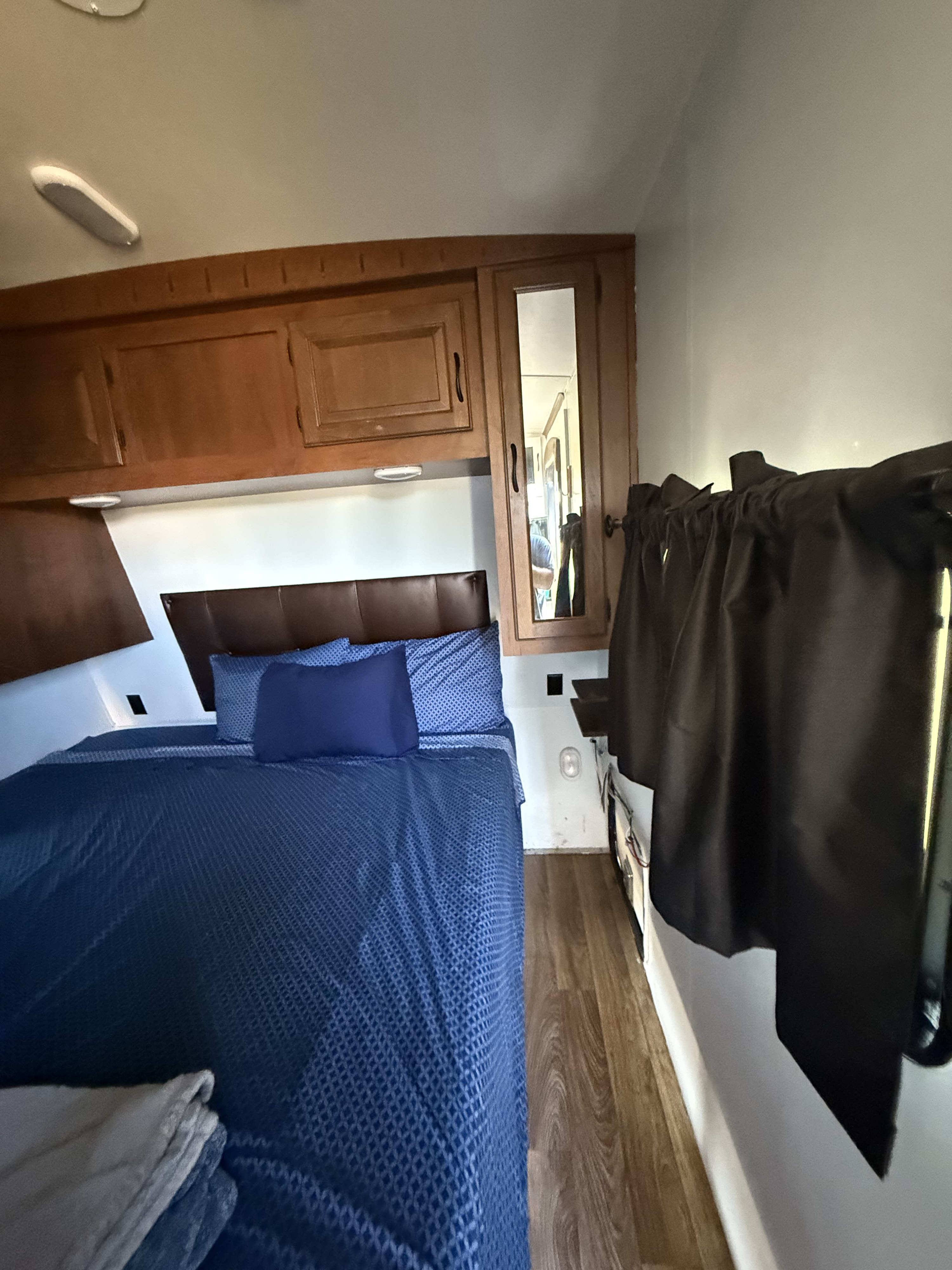 Cozy RV rental bedroom with blue-patterned bed, brown headboard, wooden cabinets, a mirror, and dark curtains.. Eagle Premier 314BHDS 2015