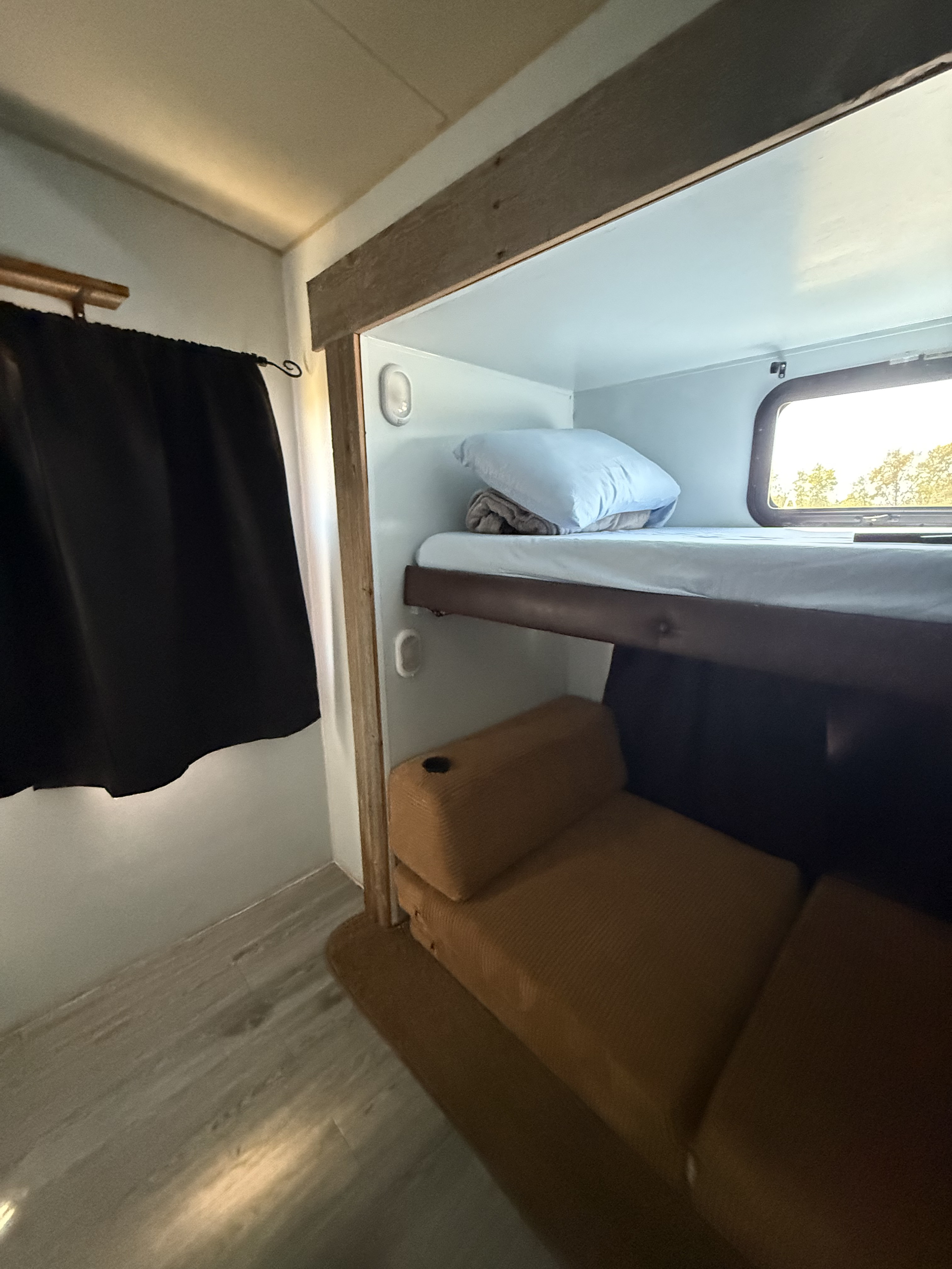 Interior of an RV rental showing stacked bunk beds, a window with outdoor scenery, and a lower lounge seat with a cup holder.. Eagle Premier 314BHDS 2015