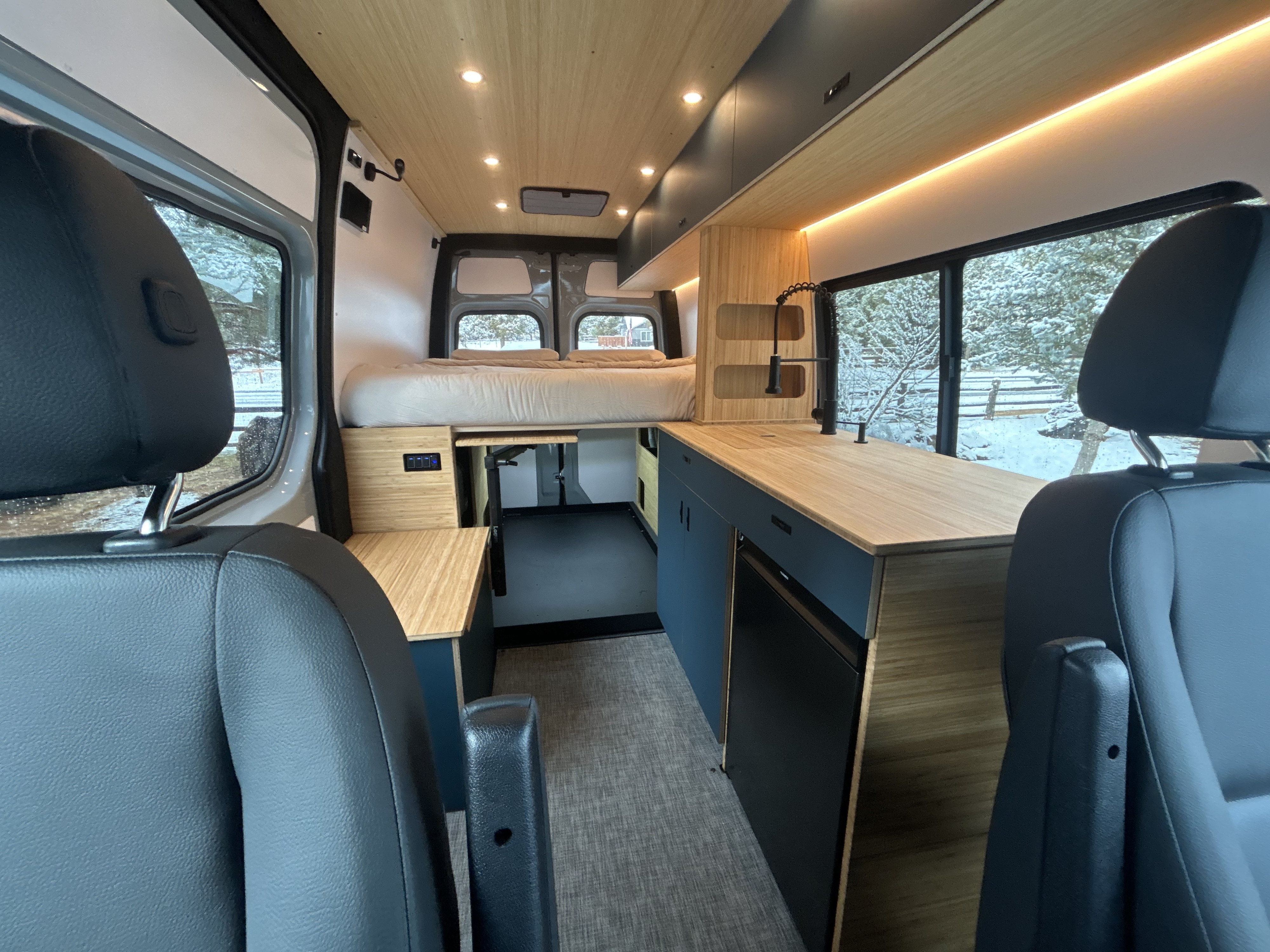 Modern RV rental interior with a cozy bed, kitchen, wood accents, and warm lighting, ready for snowy adventures.. W1Y4NBVY4ST232112 Geotrek 2025