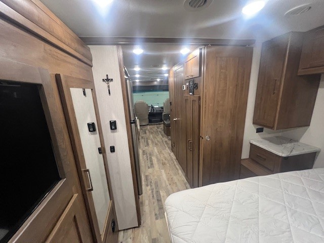 Spacious RV rental interior, showing bedroom, hallway with controls, TV, and wood cabinetry leading to the driver's cockpit.. Forest River Coachmen Pursuit 2020