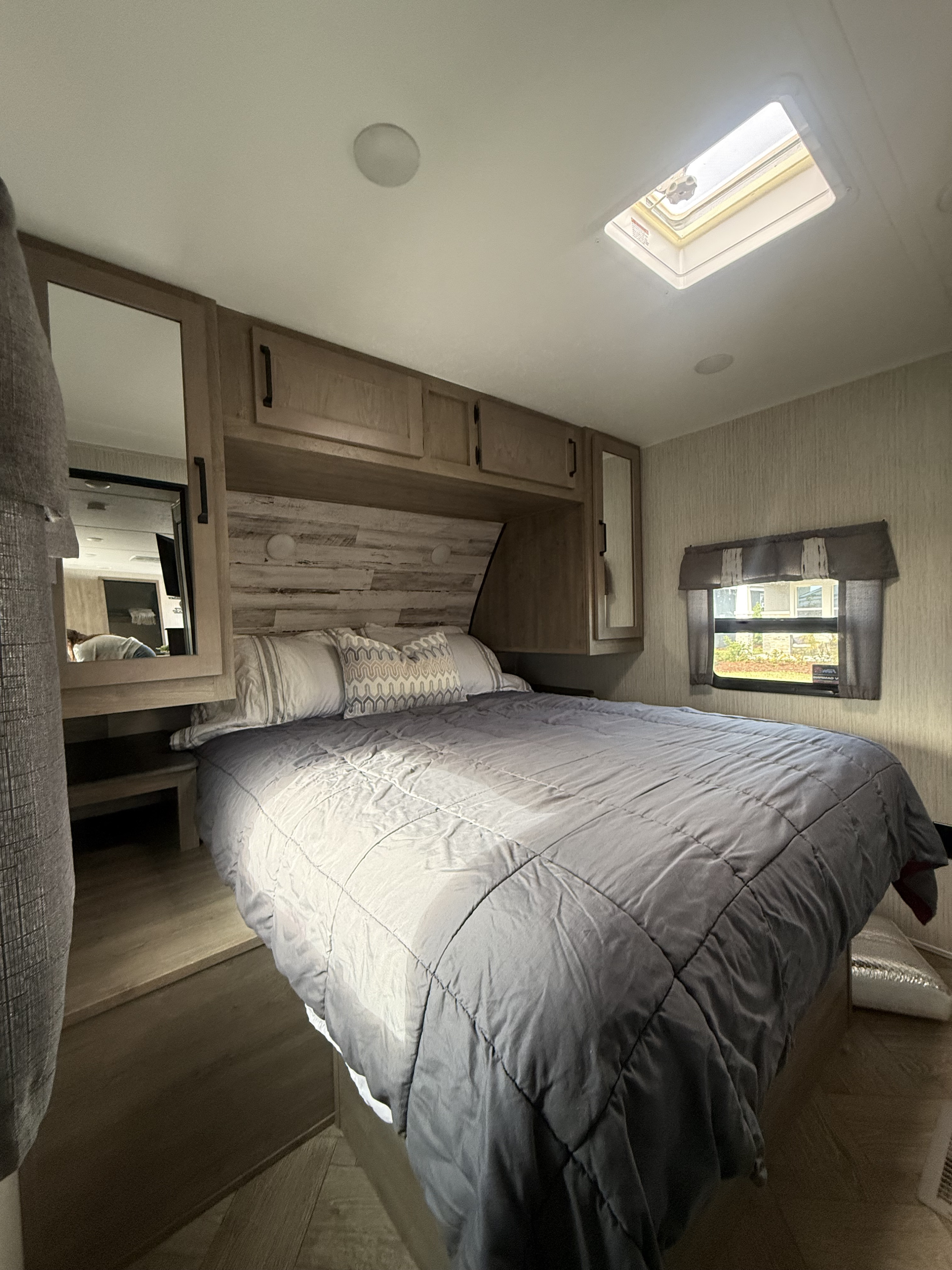 Comfortable RV rental bedroom with a cozy bed, overhead storage, side mirrors, a window with curtains, and a ceiling skylight.. Forest River Palomino Puma 2022