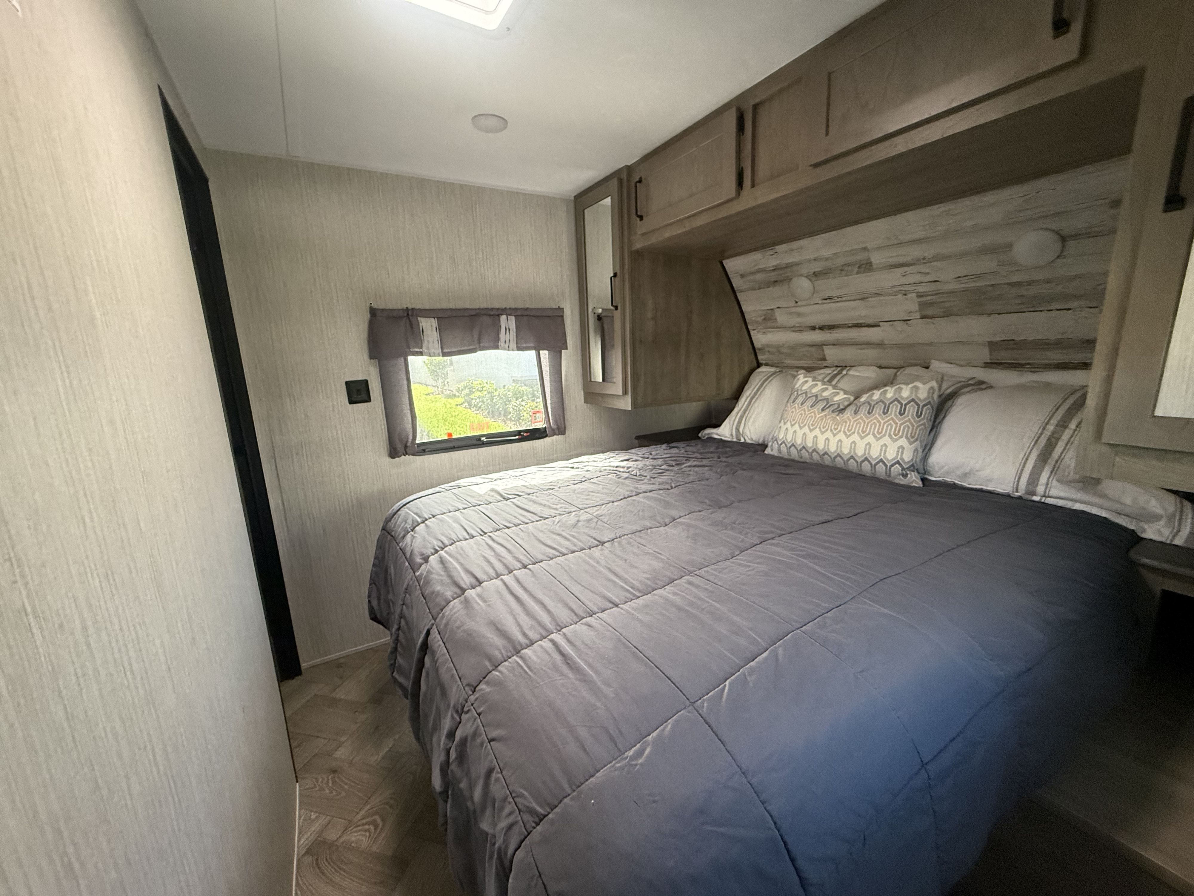 Spacious RV rental bedroom featuring a large bed, modern overhead cabinets, and a bright window. Your comfortable home on wheels.. Forest River Palomino Puma 2022
