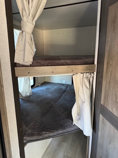 Two stacked bunk beds inside an RV rental, complete with grey bedding and individual privacy curtains for privacy.. Forest River Surveyor Legend 2022