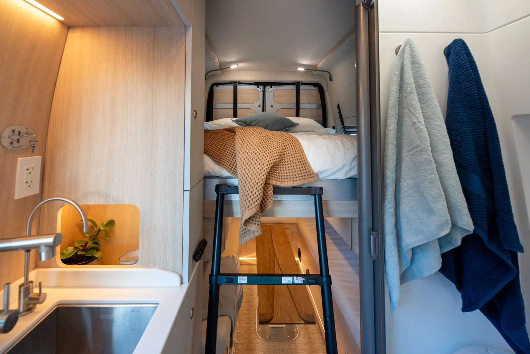 RV rental interior featuring a raised bed with ladder, compact kitchen with plant, and hanging towels.. Noovo Noovo Class B 2025