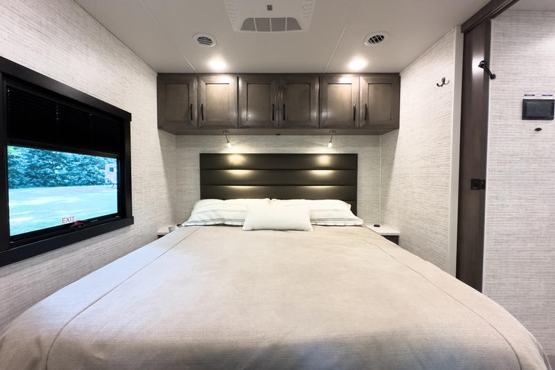 RV rental bedroom interior featuring a comfortable bed, overhead cabinets, and a window with outdoor views.. Jayco Precept 2022