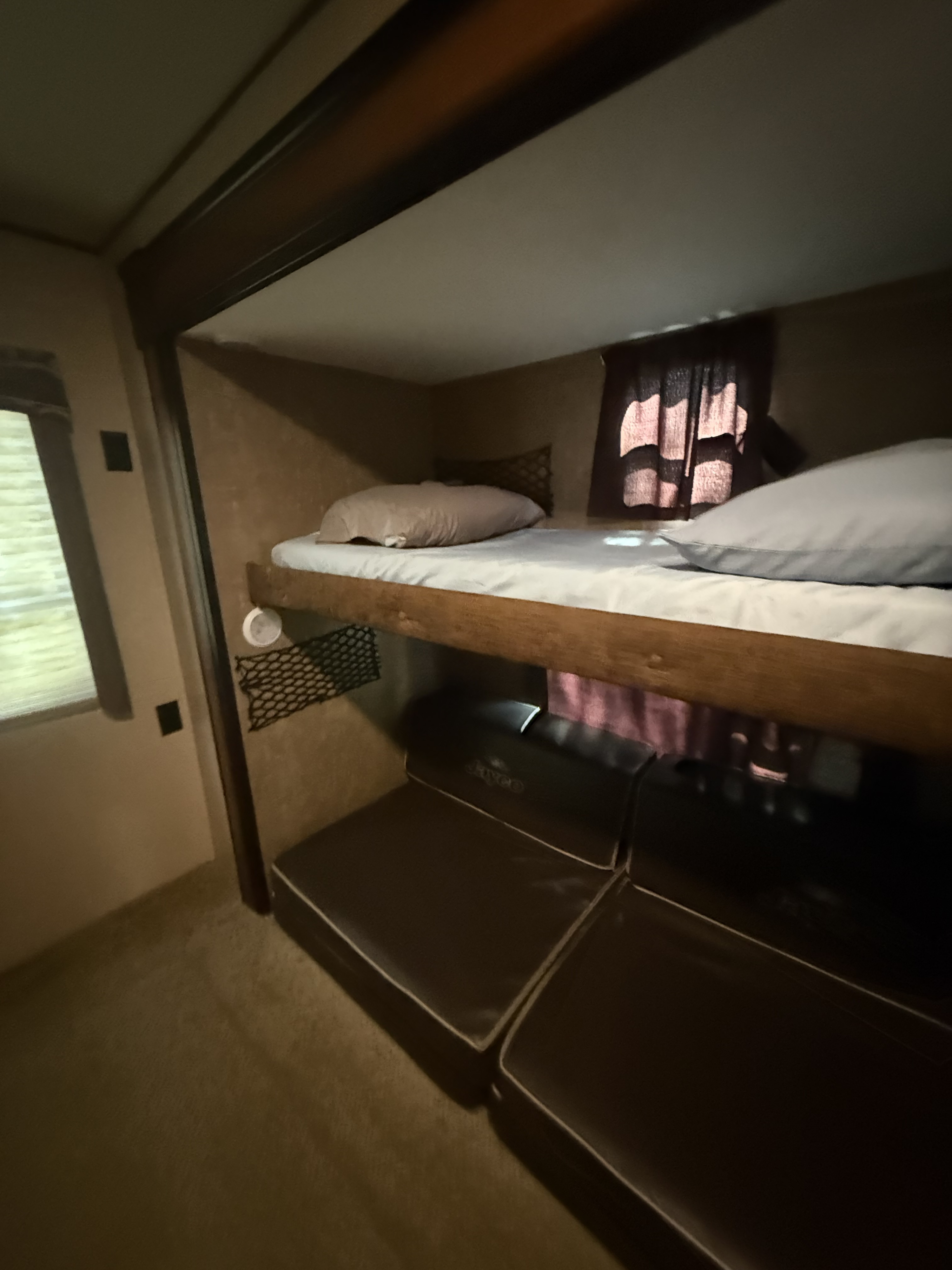 Explore this RV rental's interior: a snug bunk bed with pillows and sheets above dark brown seating cushions, illuminated by a window.. Jay Flight 32BHDS 2016