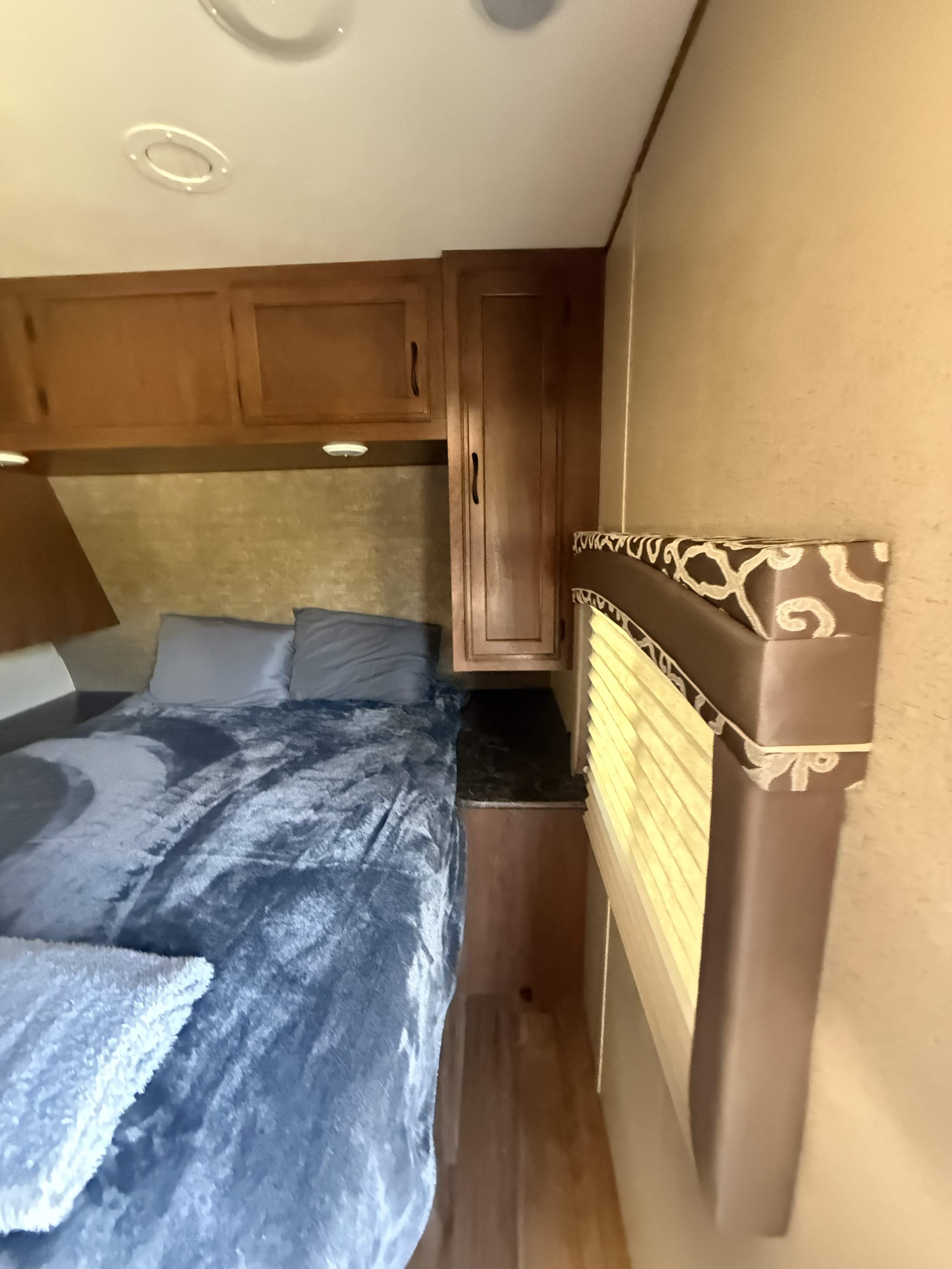 Cozy RV rental bedroom with a plush blue bed, wooden overhead cabinets, and a decorative window valance. Ideal for road trip comfort.. Jay Flight 32BHDS 2016