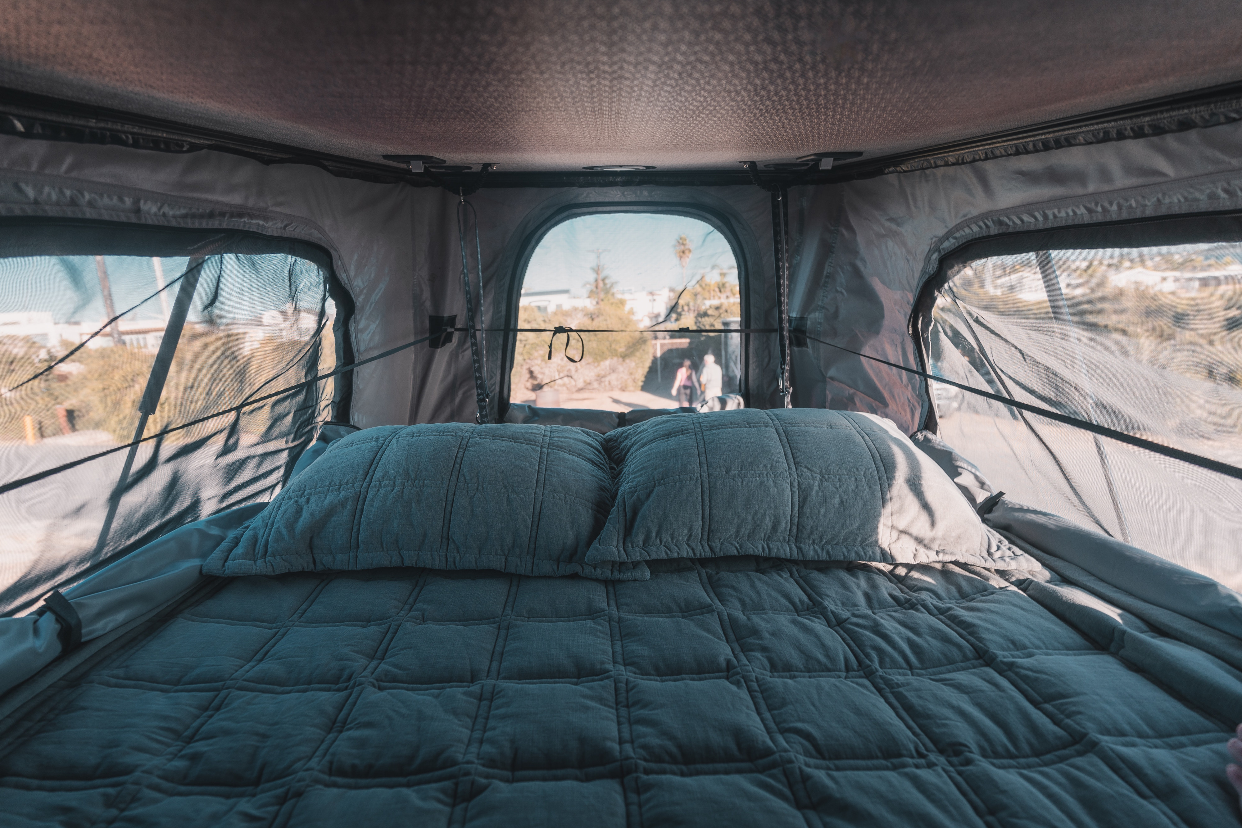 Cozy rv rental interior: A quilted bed with pillows inside a rooftop tent, offering scenic outdoor views through screened windows.. Winnebago Solis 2025