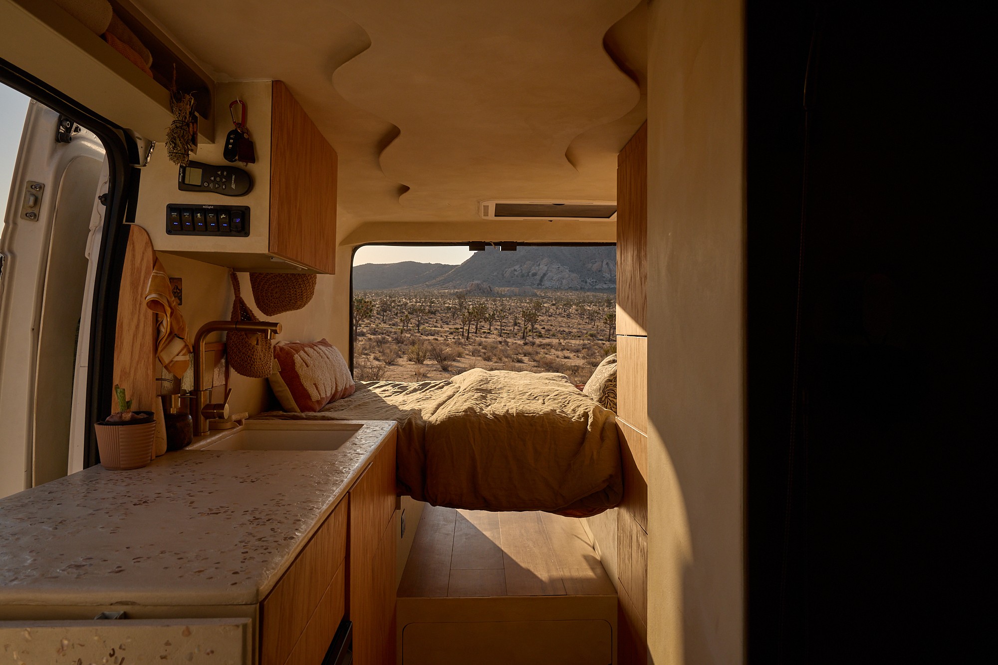 Cozy RV rental interior: A modern camper van with a bed, kitchen, and a desert view through the back window.. Dodge Ram 1500 2021