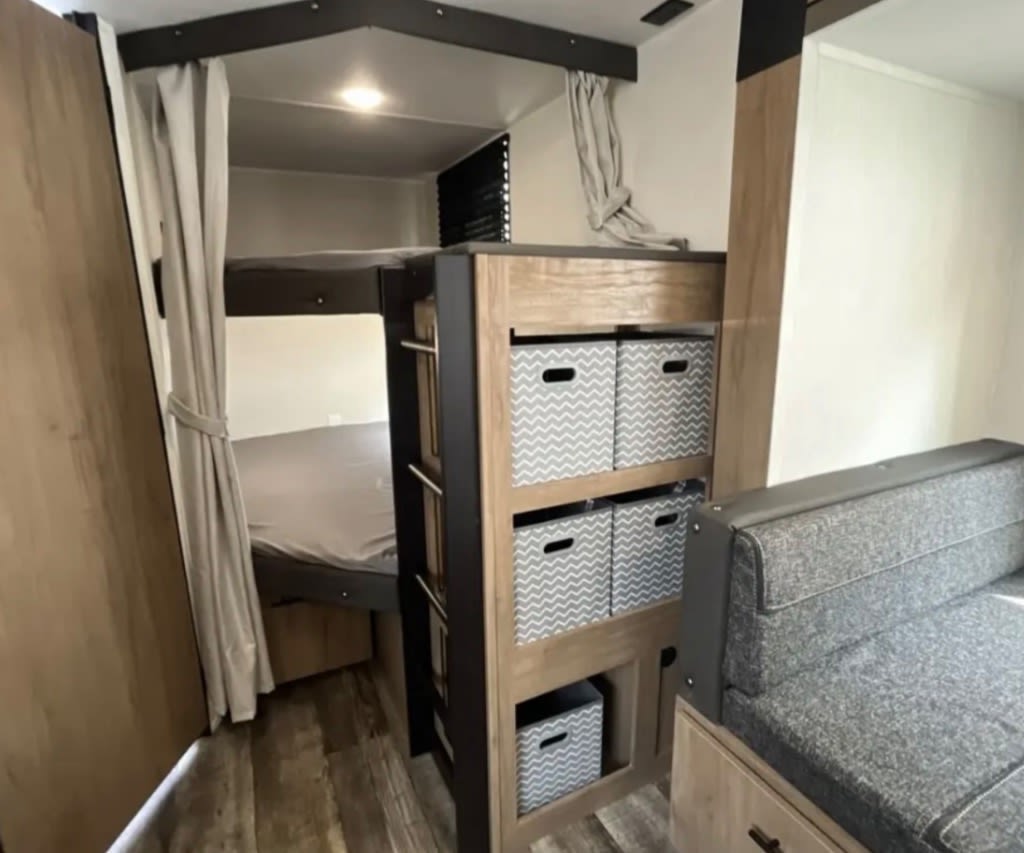 RV rental: Bunk beds, chevron storage bins, and comfy sofa. A compact, functional camper interior with wood-look flooring.. Forest River Campsite Reserve 2025