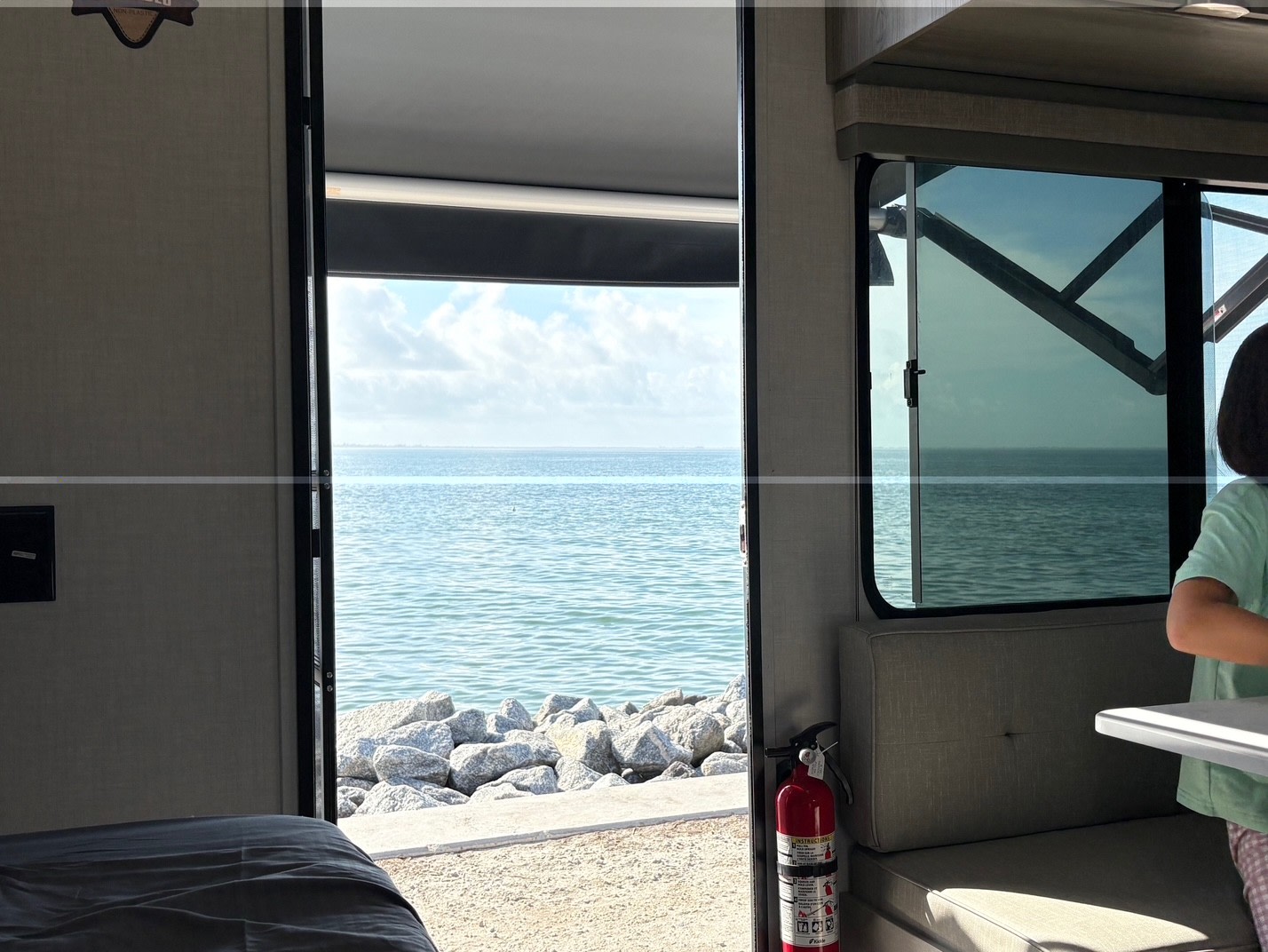 An RV rental provides stunning ocean views from its comfortable interior, featuring a bed and dinette, overlooking a rocky shore.. Forest River Salem FSX 2025