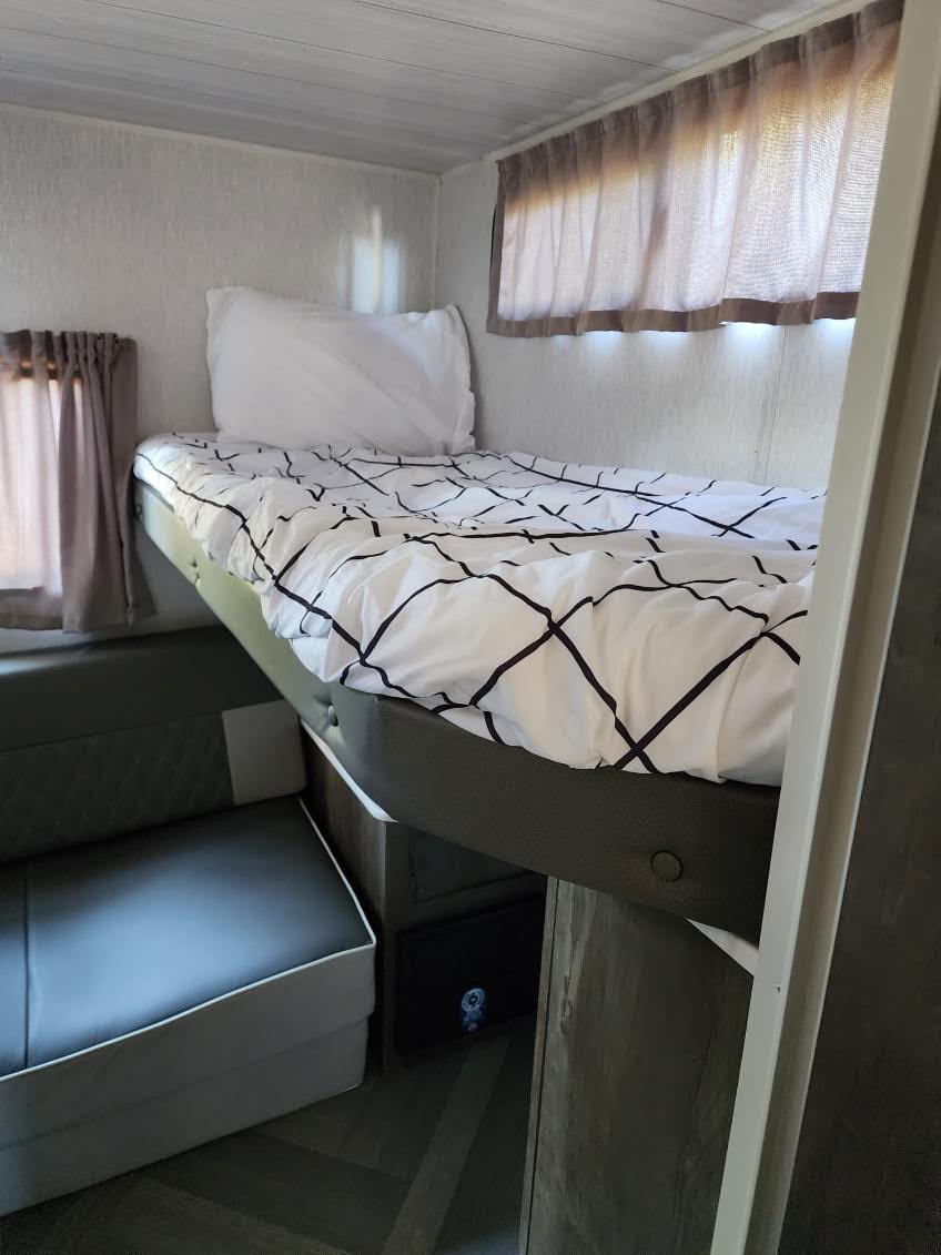 Compact RV rental interior with a cozy bunk bed, patterned bedding, white pillow, and upholstered bench seating below.. Forest River Salem 2022