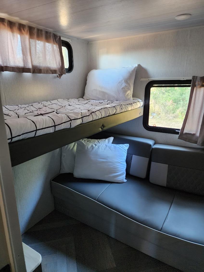 Inside an rv rental: a comfy bunk bed with patterned bedding and a sofa for relaxing, featuring windows and curtains.. Forest River Salem 2022