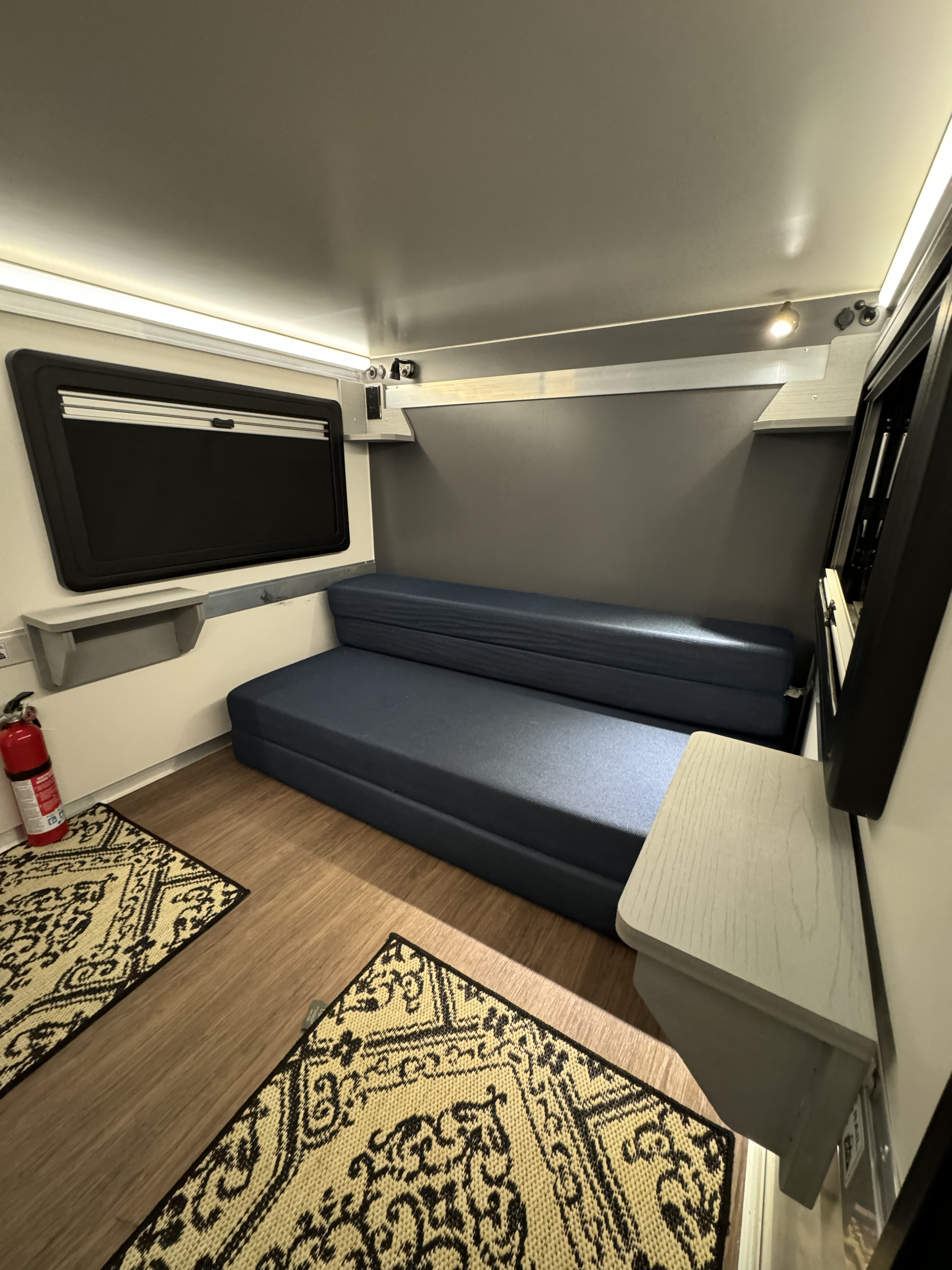 Bright rv rental interior features a blue convertible sofa, window, and wood floor with rugs. Compact & functional space.. Core RV Core RV 5510 2024