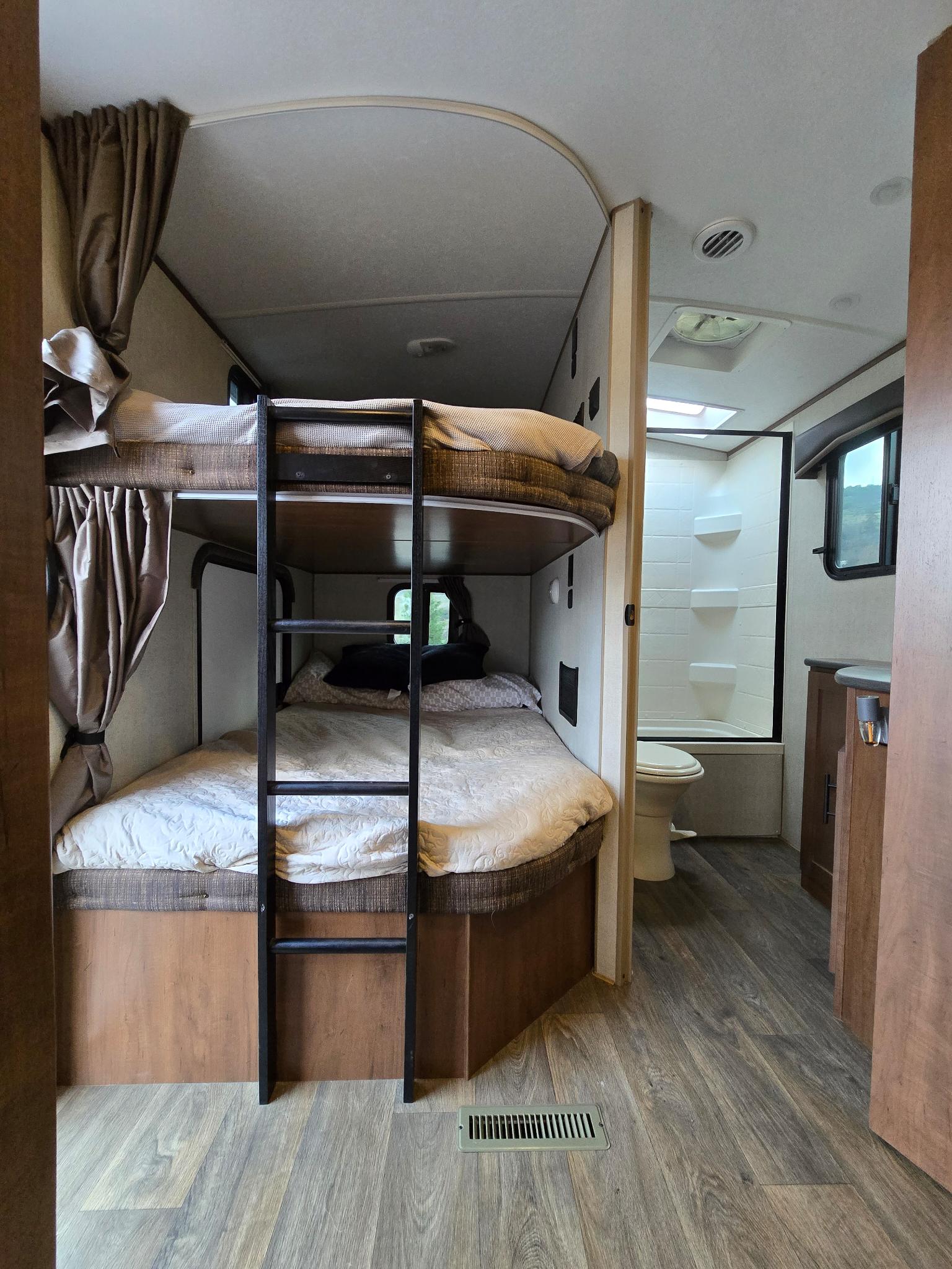 An RV rental interior: bunk beds with ladder, adjacent compact bathroom with toilet & shower. Wood-look floors.. Outdoors RV Timber Ridge 2024
