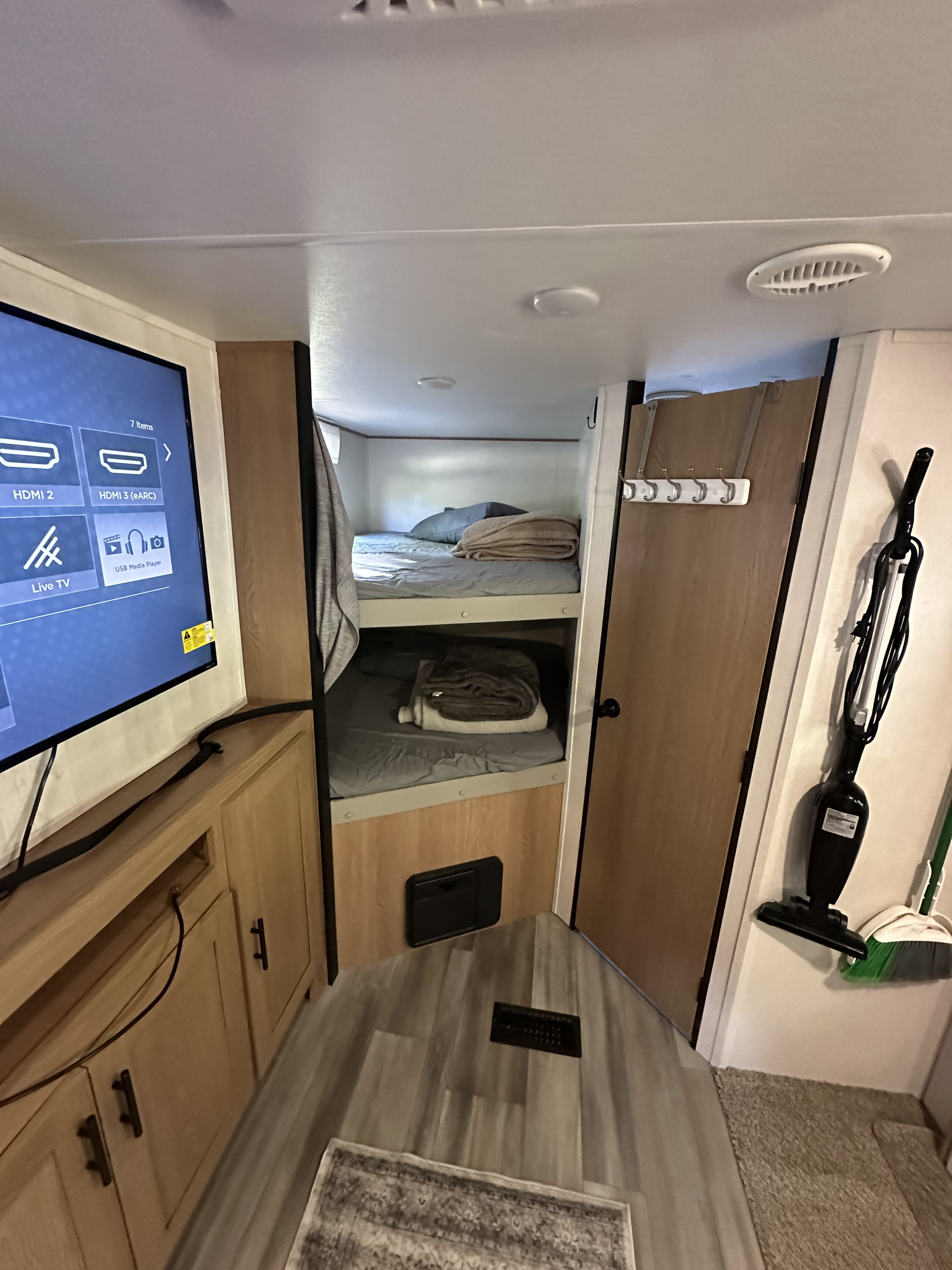Cozy rv rental interior featuring bunk beds, a TV with media options, and compact cleaning storage for a comfortable journey.. Avenger Avenger Trailer 2022