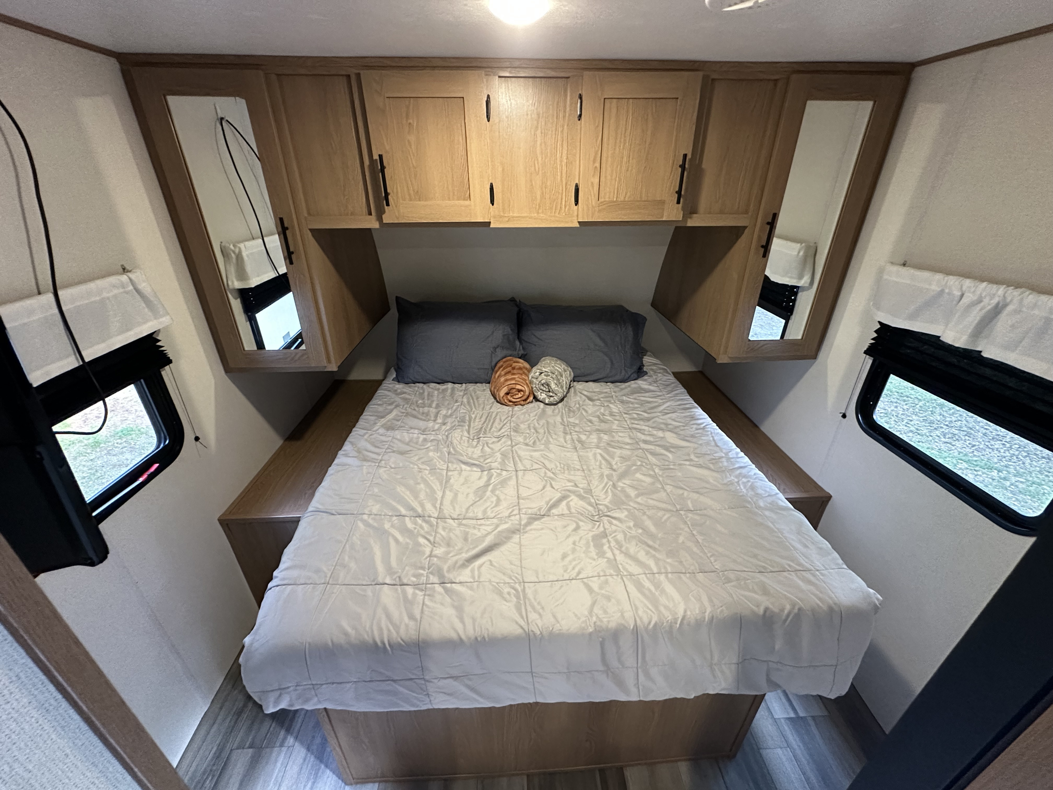 Bright RV rental bedroom featuring a queen bed, wooden overhead cabinets, and side windows with shades, ready for a comfortable night.. Avenger Avenger Trailer 2022