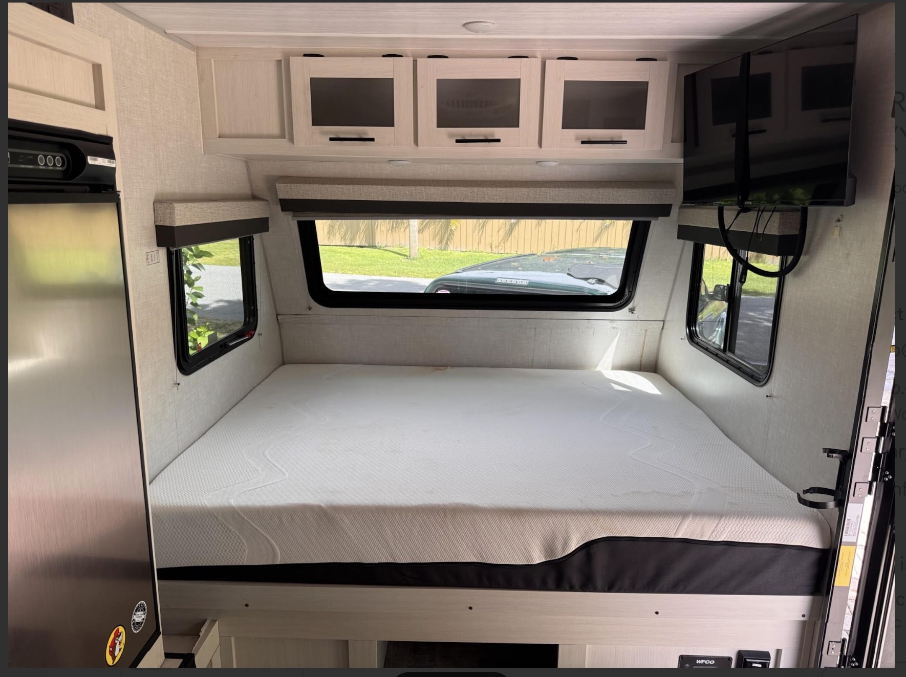 Cozy RV rental bedroom interior with a large bed, overhead storage, TV, and refrigerator. Light-toned finishes.. Forest River No Boundaries NoBo 16.6 2023