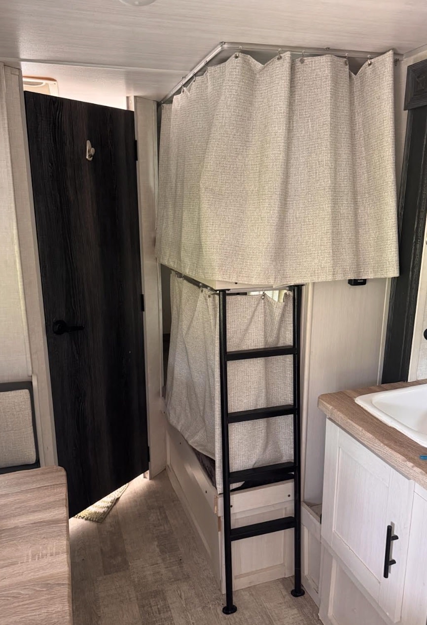 Cozy RV rental interior with bunk beds, privacy curtains, ladder, a dark door, and a small sink area.. Forest River No Boundaries NoBo 16.6 2023