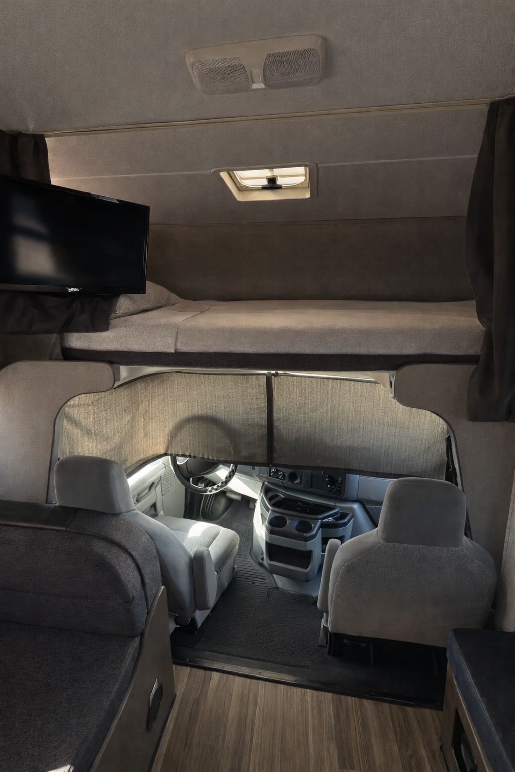 View inside an rv rental: cozy over-cab bunk with TV, front cab seating, and window shades in a camper's interior.. Thor Majestic 2018