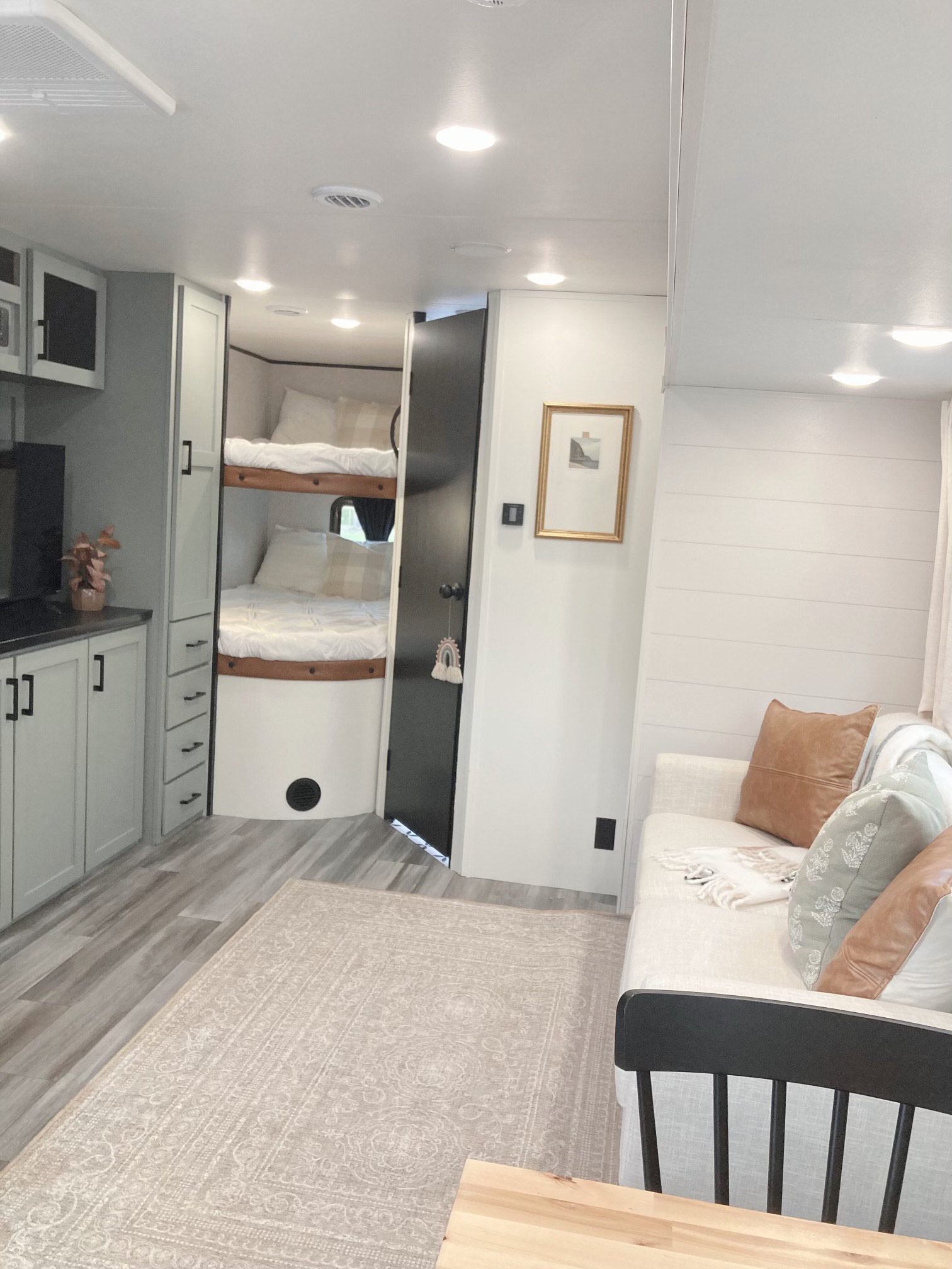 Bright RV rental interior: light wood floors, cozy bunk beds, soft sofa with pillows, and modern light grey cabinetry. Travel ready!. Jayco Jay Flight SLX 2025