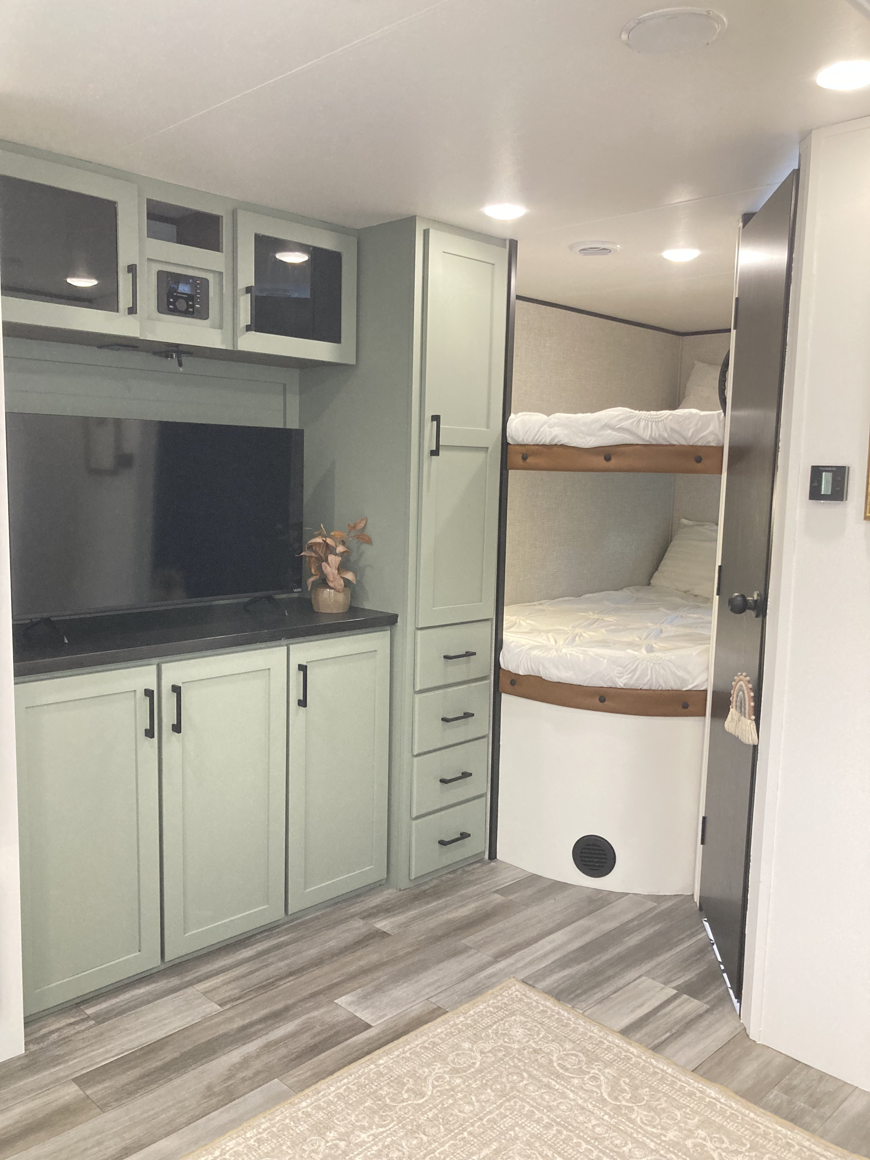 Modern RV rental interior featuring light green cabinetry, an entertainment center, and cozy bunk beds with white bedding.. Jayco Jay Flight SLX 2025