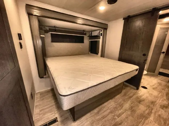 Spacious RV rental bedroom with a large bed, built-in headboard storage, and modern barn door. Cozy interior for travel.. Keystone RV Montana 2023