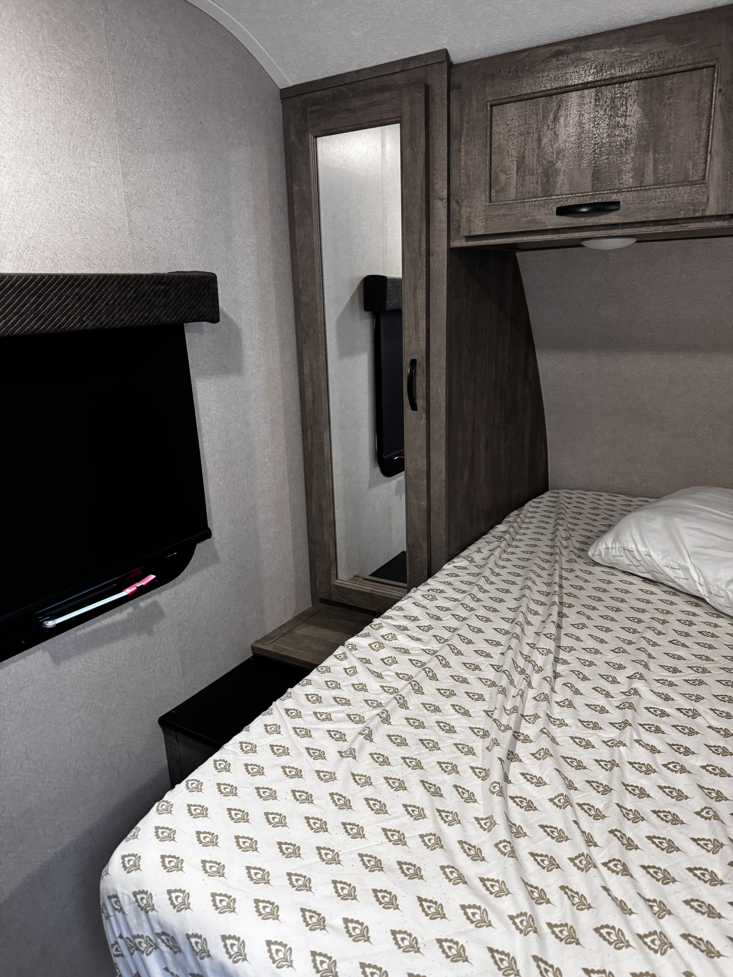 Inside a compact RV rental bedroom, featuring a patterned bed, wall-mounted TV, and a mirrored wardrobe for convenient storage.. Forest River Vibe 2020