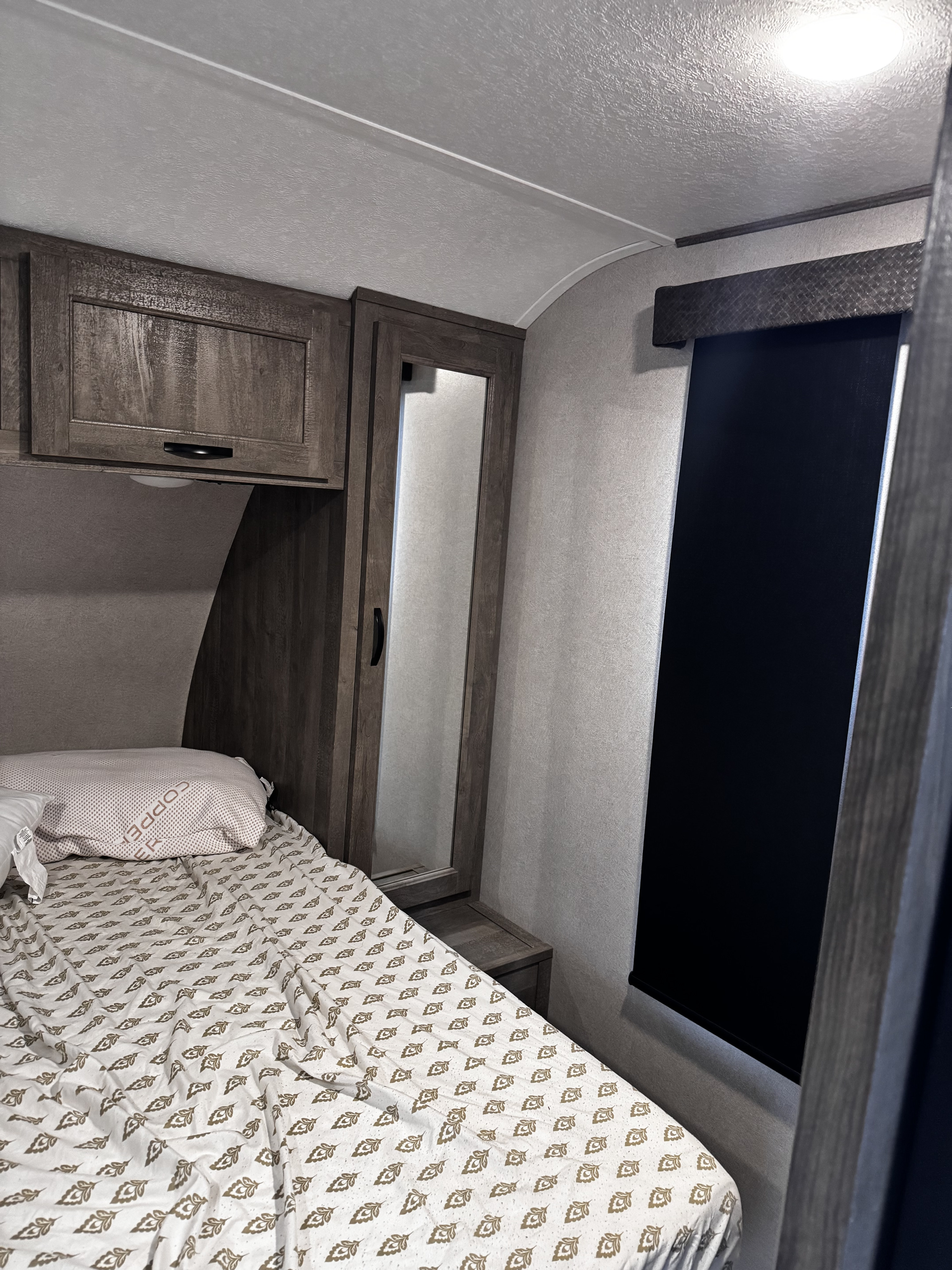 RV rental bedroom: compact bed with patterned sheets, wood cabinets, mirror, and blackout window shade.. Forest River Vibe 2020