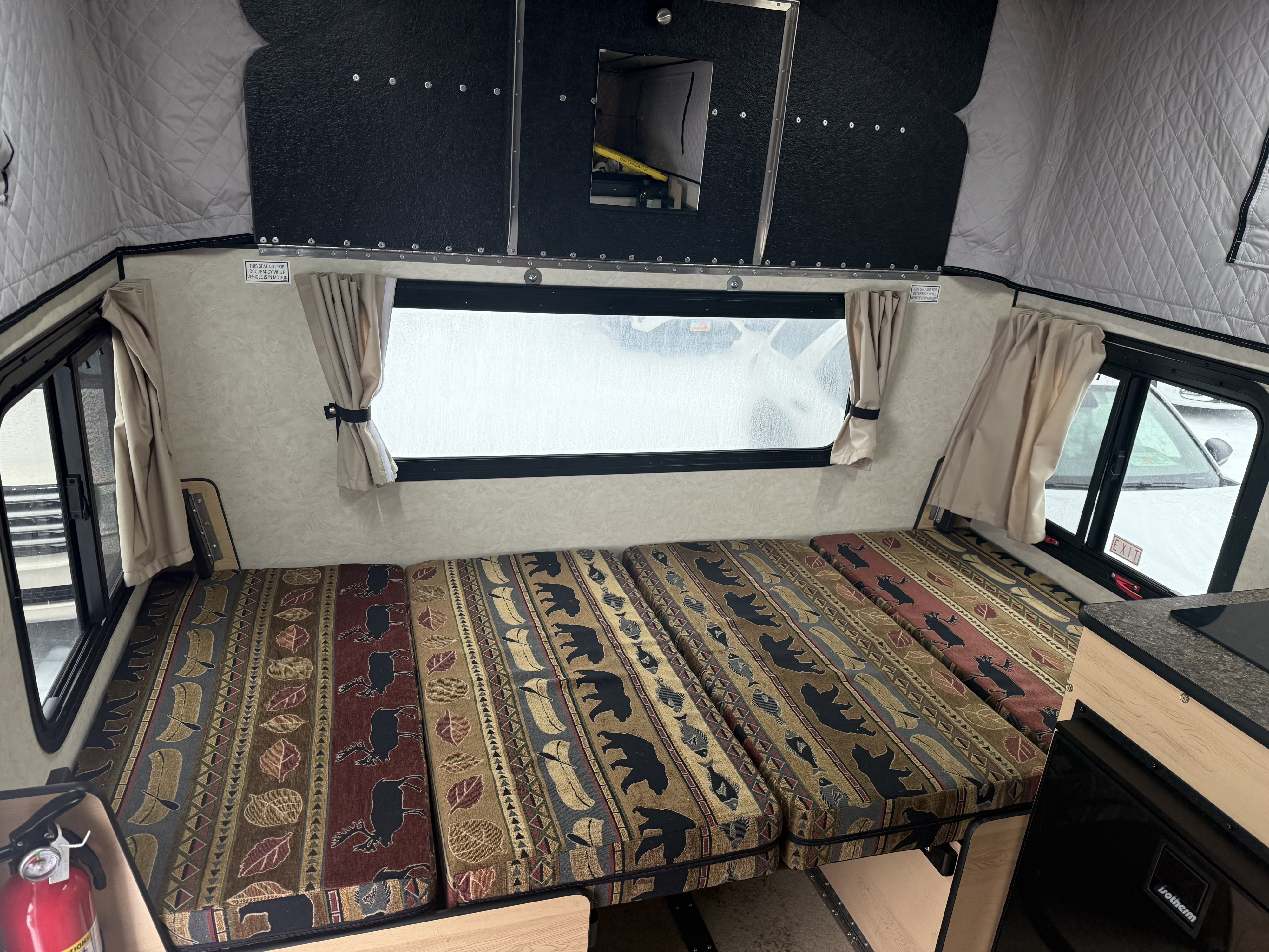 Explore this rv rental camper interior: comfy seats/bed with wilderness patterns, windows, and compact kitchenette.. Four Wheel Campers Hawk + 2026