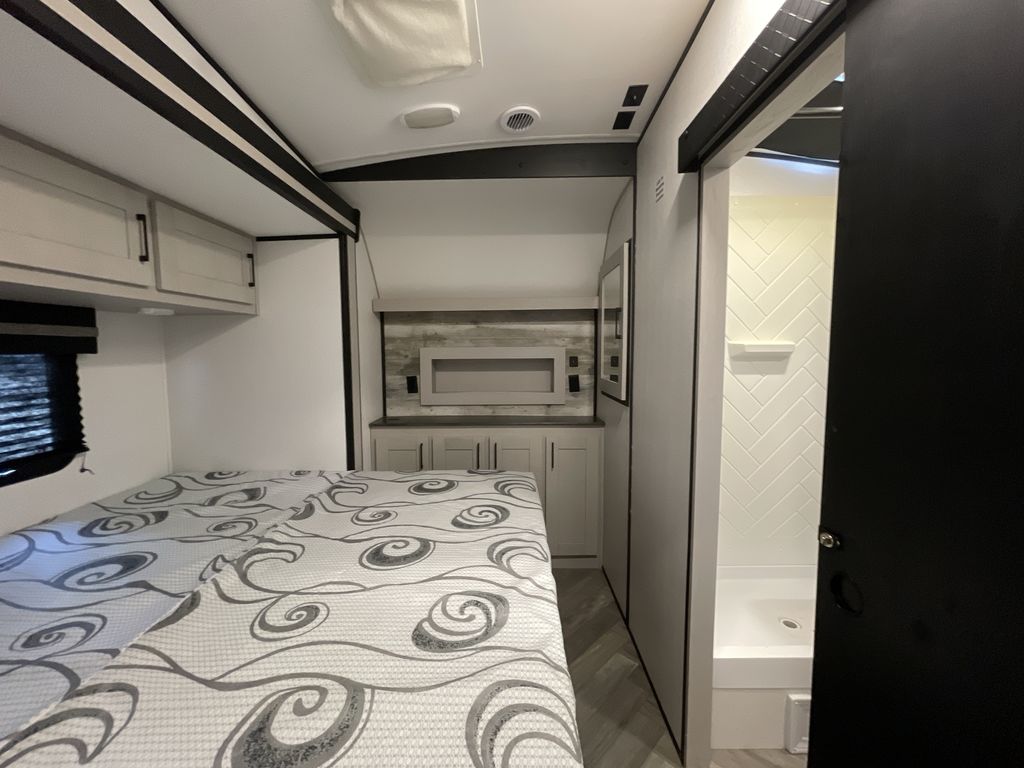 Modern RV rental bedroom with patterned bed, overhead cabinets, and attached bathroom with herringbone shower tiles.. Heartland Torque 2022