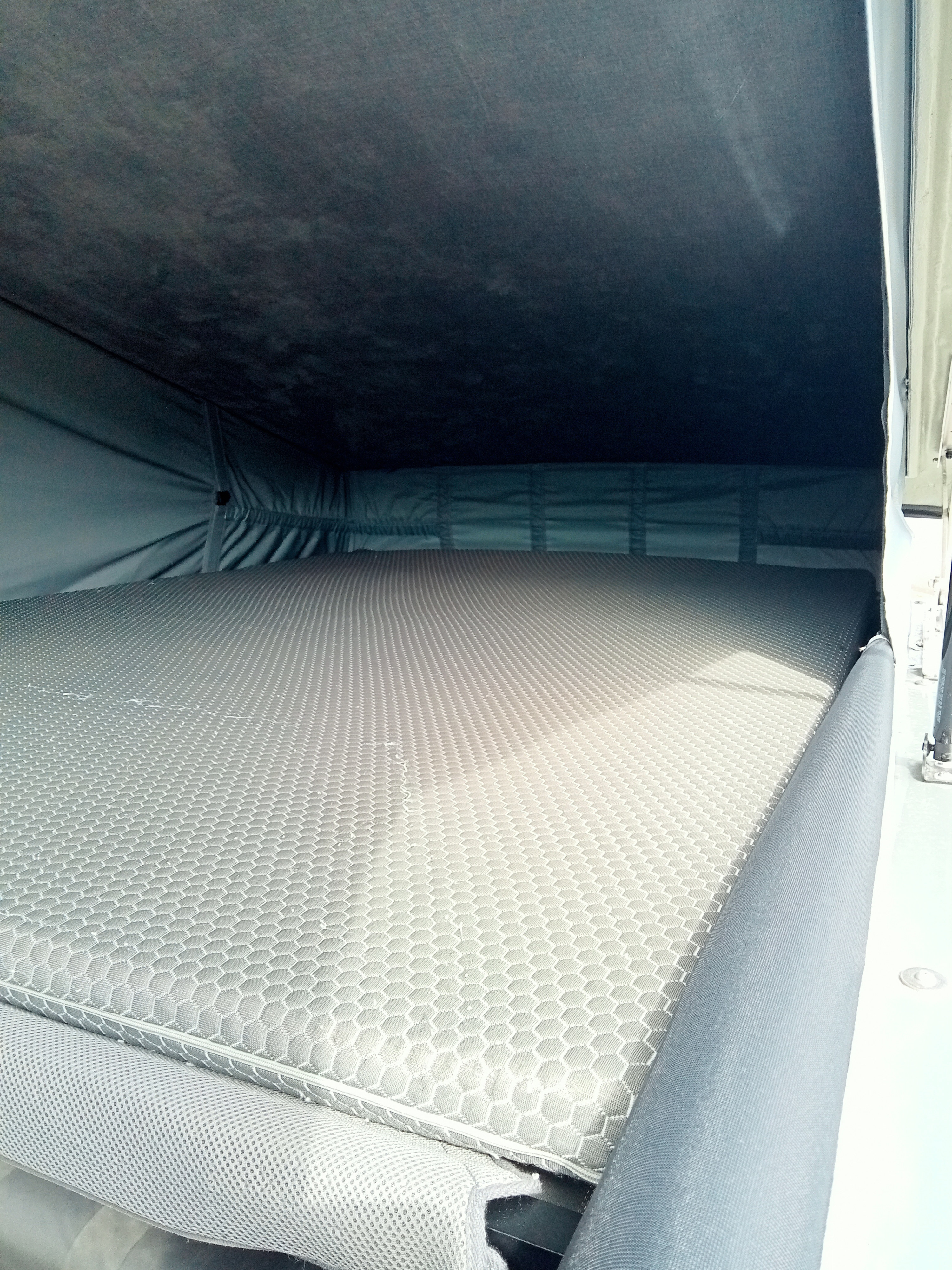 Inside this RV rental, a comfy bed with a light grey, honeycomb-patterned mattress awaits for camping comfort.. Renault Trafic 2025
