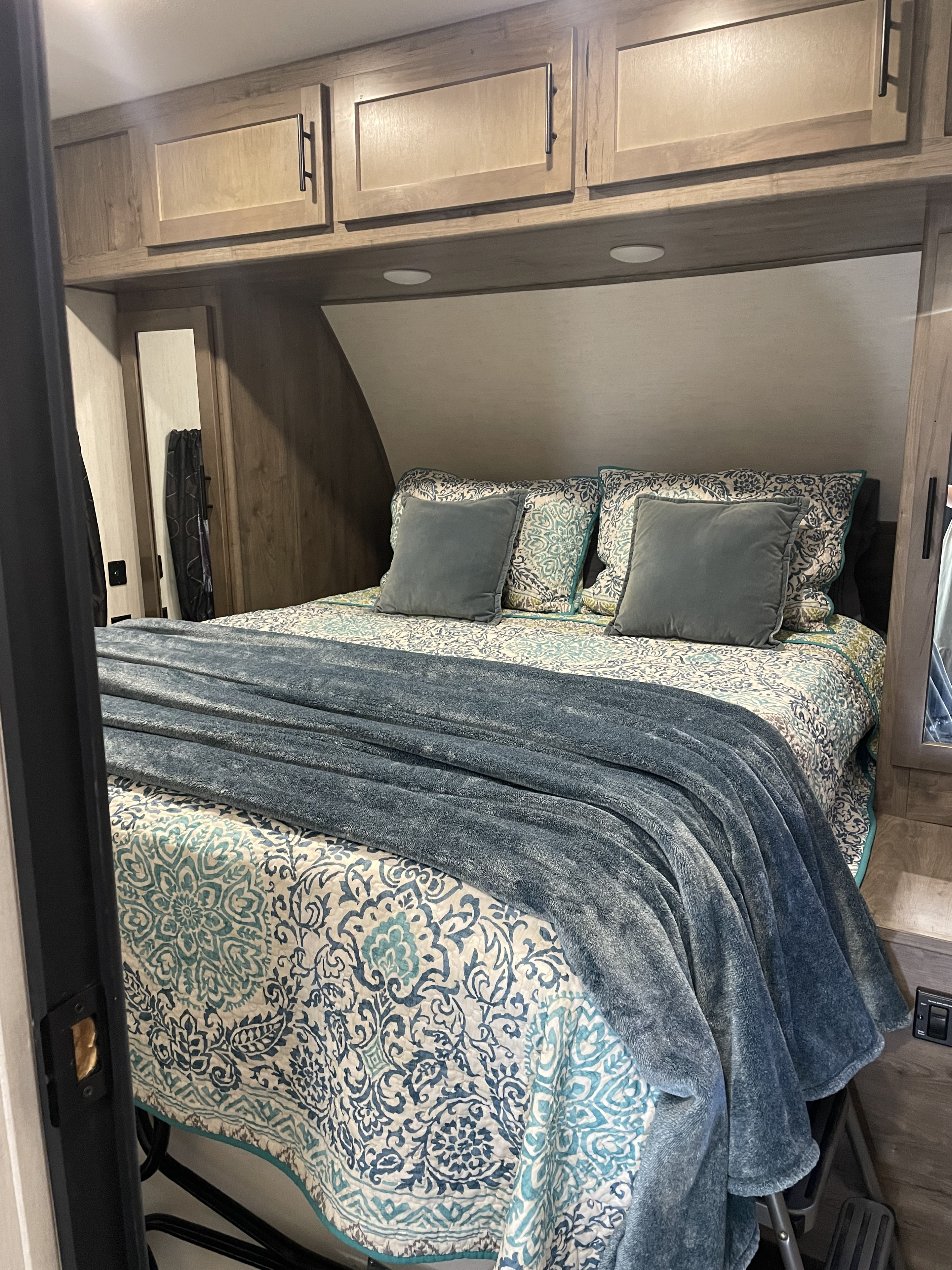 Cozy bedroom inside an rv rental, featuring a patterned quilt, blue blanket, and overhead cabinets for storage.. Forest River Cherokee Wolf Pack 2021