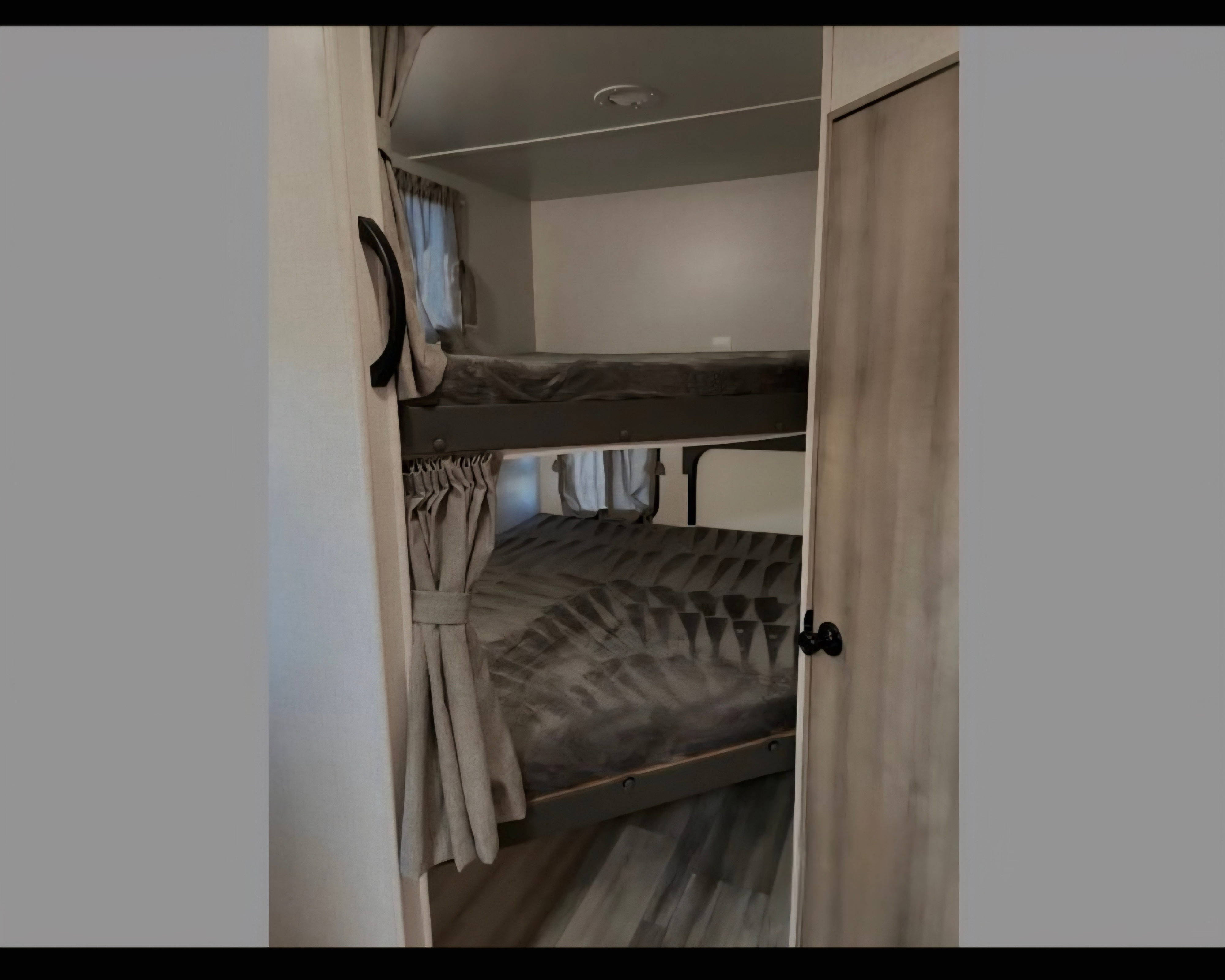Cozy bunk beds inside an rv rental, featuring private curtains and comfortable grey bedding for a restful sleep.. Winnebago Voyage 2022