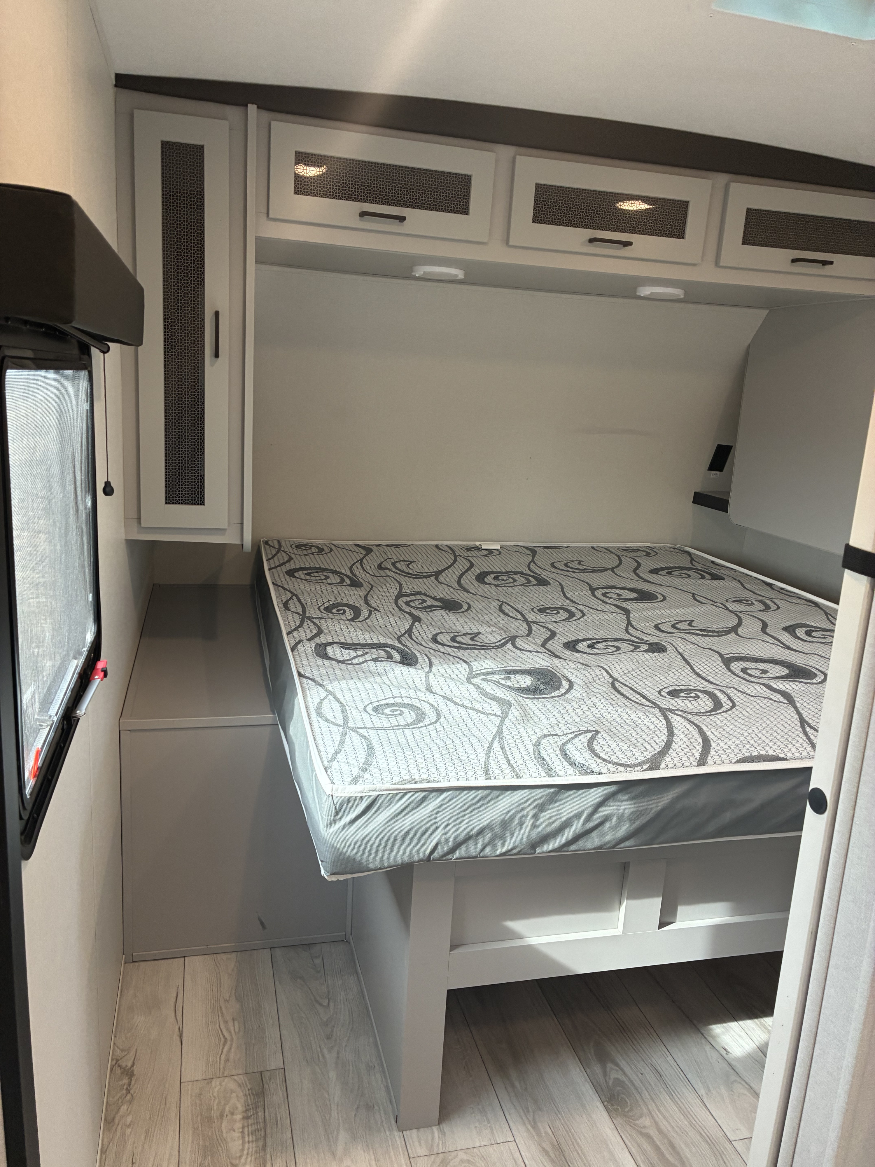 Cozy RV rental bedroom featuring a patterned bed, modern overhead cabinets, and wood-look flooring for your adventures.. Heartland RVs North Trail 2024