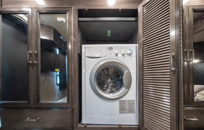 RV rental interior: A compact front-load washing machine in a dark wood cabinet, with mirrored and louvered doors.. Fleetwood Pace Arrow 35E 2019