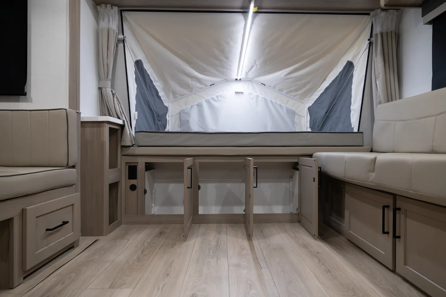 Modern RV rental interior with a pop-up bed, open storage cabinets below, and comfortable dinette seating on a light wood floor.. Forest River Rockwood Roo 2022