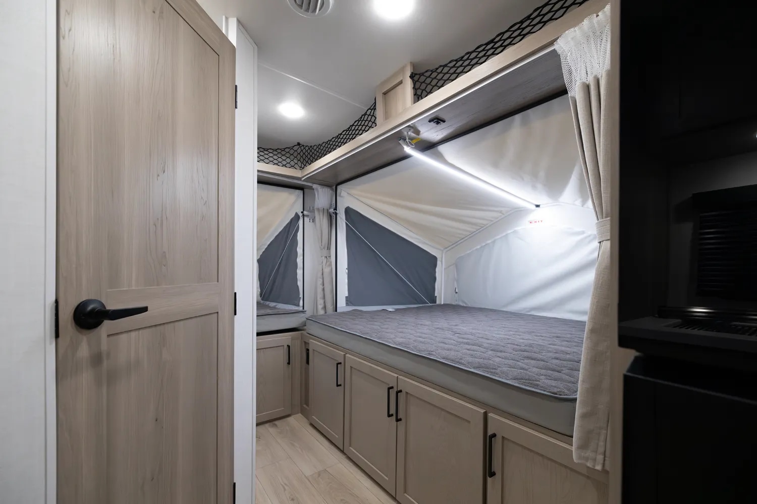 Modern RV rental interior featuring a cozy pop-out bed with under-bed storage, overhead netting, and bright lighting.. Forest River Rockwood Roo 2022