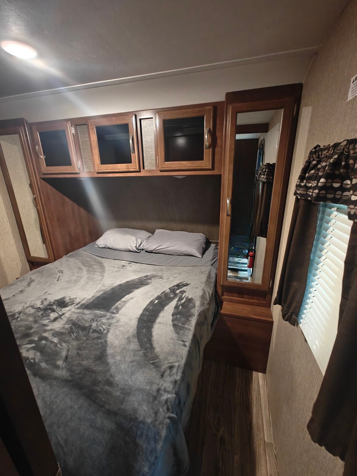 Experience comfort in this RV rental bedroom with a large bed, grey bedding, wooden overhead cabinets, and a full-length mirror.. Passport 2400BH 2017