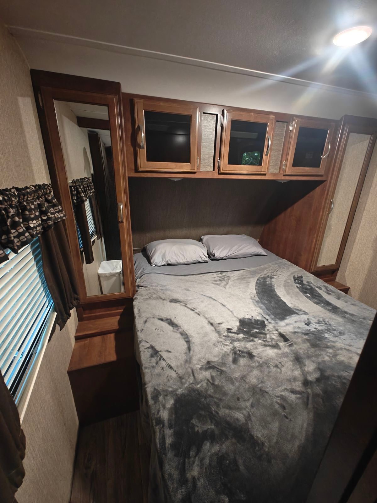 Compact RV rental bedroom with a comfy bed, mirrored wardrobe, and practical overhead storage cabinets. Bright light above.. Passport 2400BH 2017