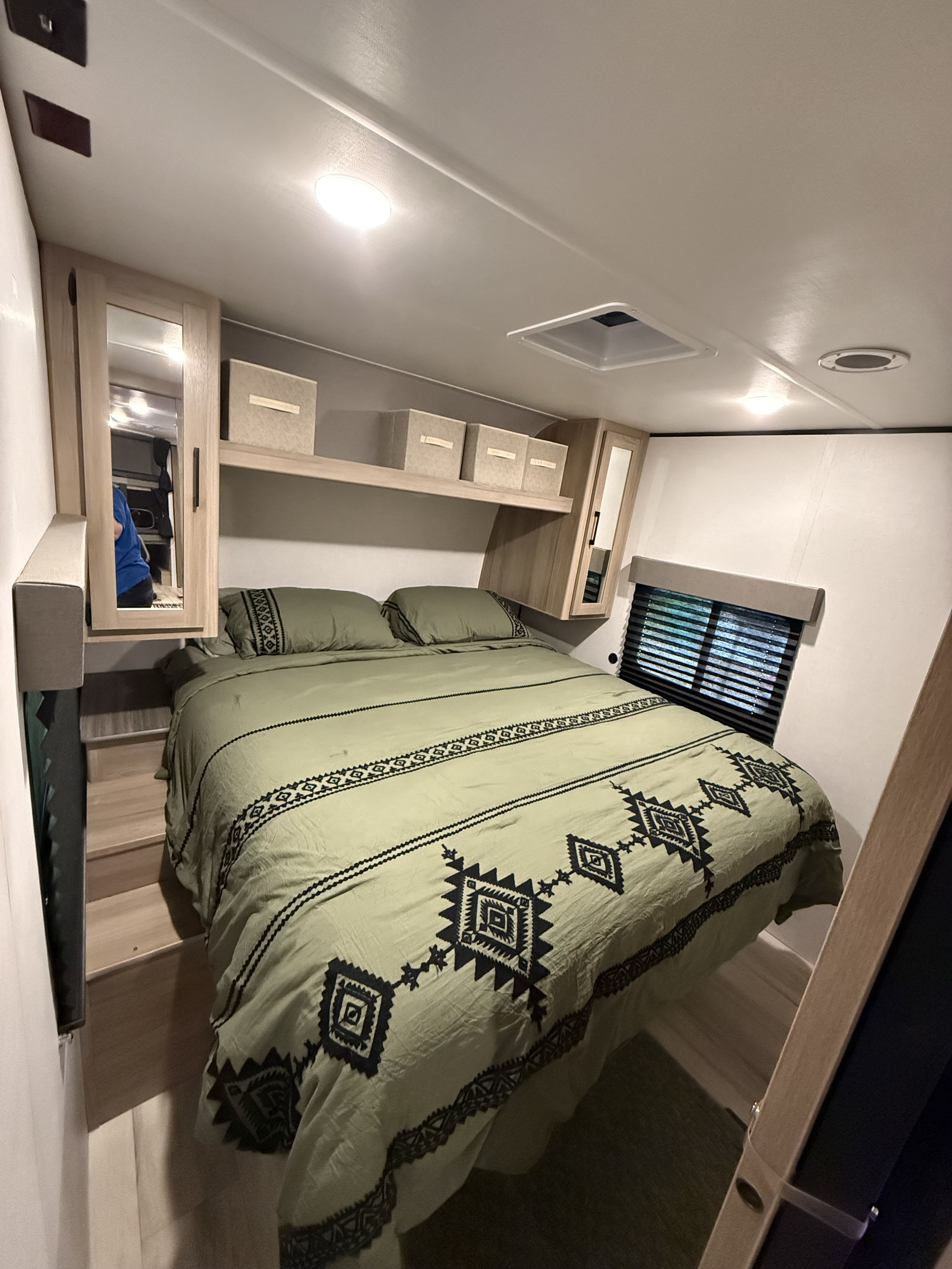 Cozy RV rental bedroom featuring a green patterned comforter, built-in storage, and steps leading to the comfortable bed.. Keystone RV Coleman Lantern 2025