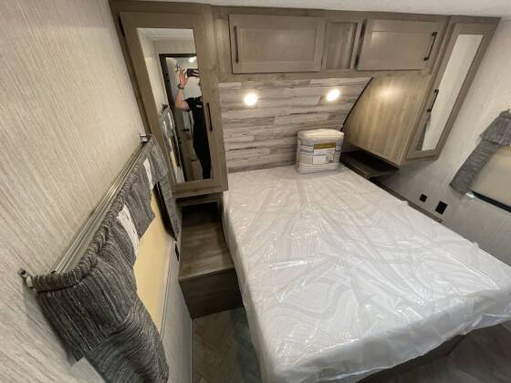 Comfortable **rv rental** bedroom featuring a plastic-covered mattress, overhead cabinets, and a side mirror. Ready for your trip.. Palomino 28bhss 2020