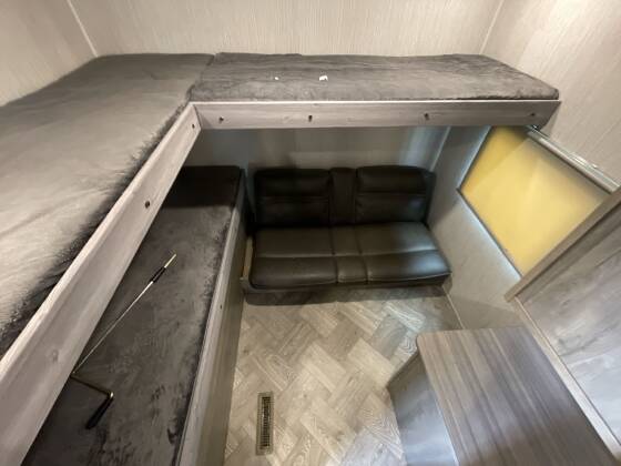 Inside this RV rental: an L-shaped bunk bed, sofa, and lower bunk/storage, with a window and wood-look flooring.. Palomino 28bhss 2020