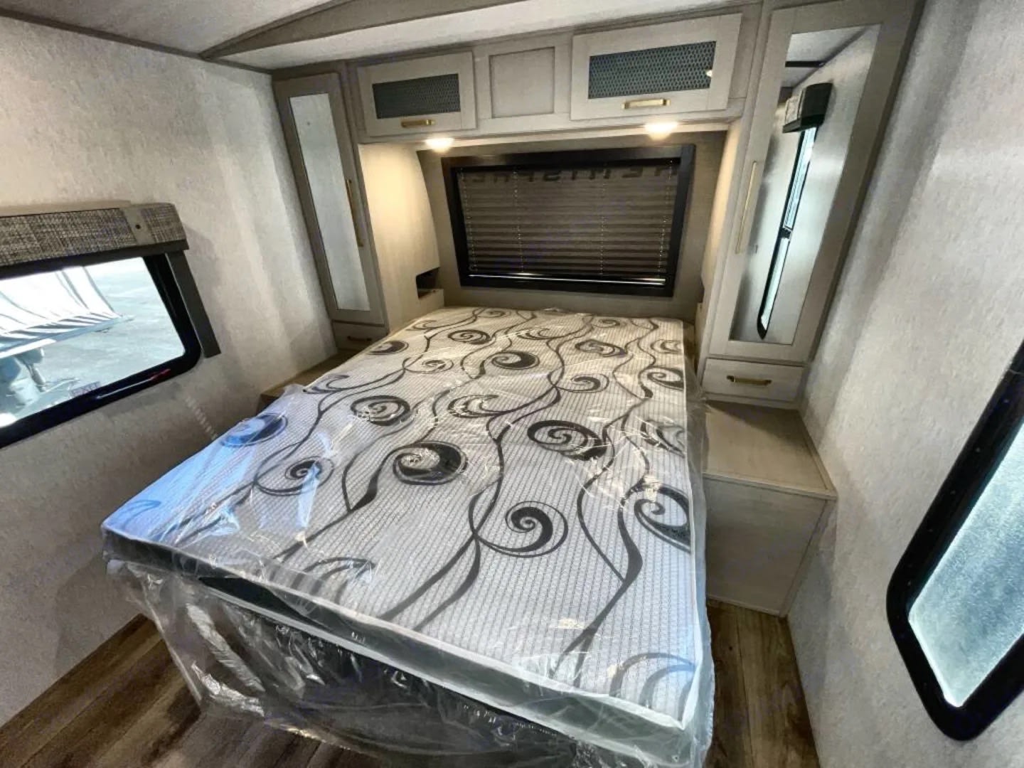 Bright RV rental bedroom: patterned bed, overhead storage, mirrored cabinets, and windows on light wood-look floor.. Forest River Salem Hemisphere 2023