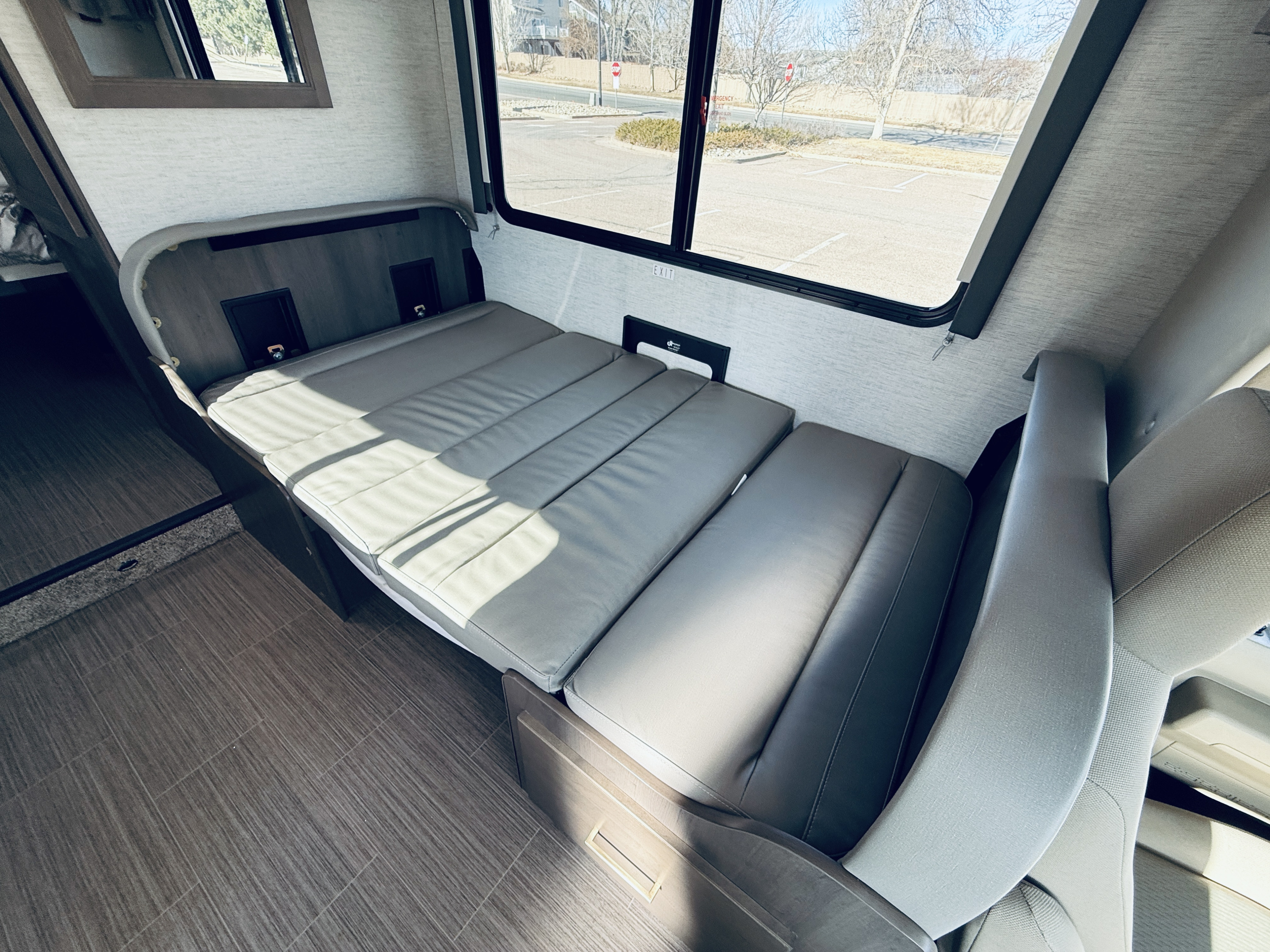 RV rental interior: gray upholstered convertible bed/seating by a large window, with tiled flooring and a mirror.. Thor Freedom Elite 2025