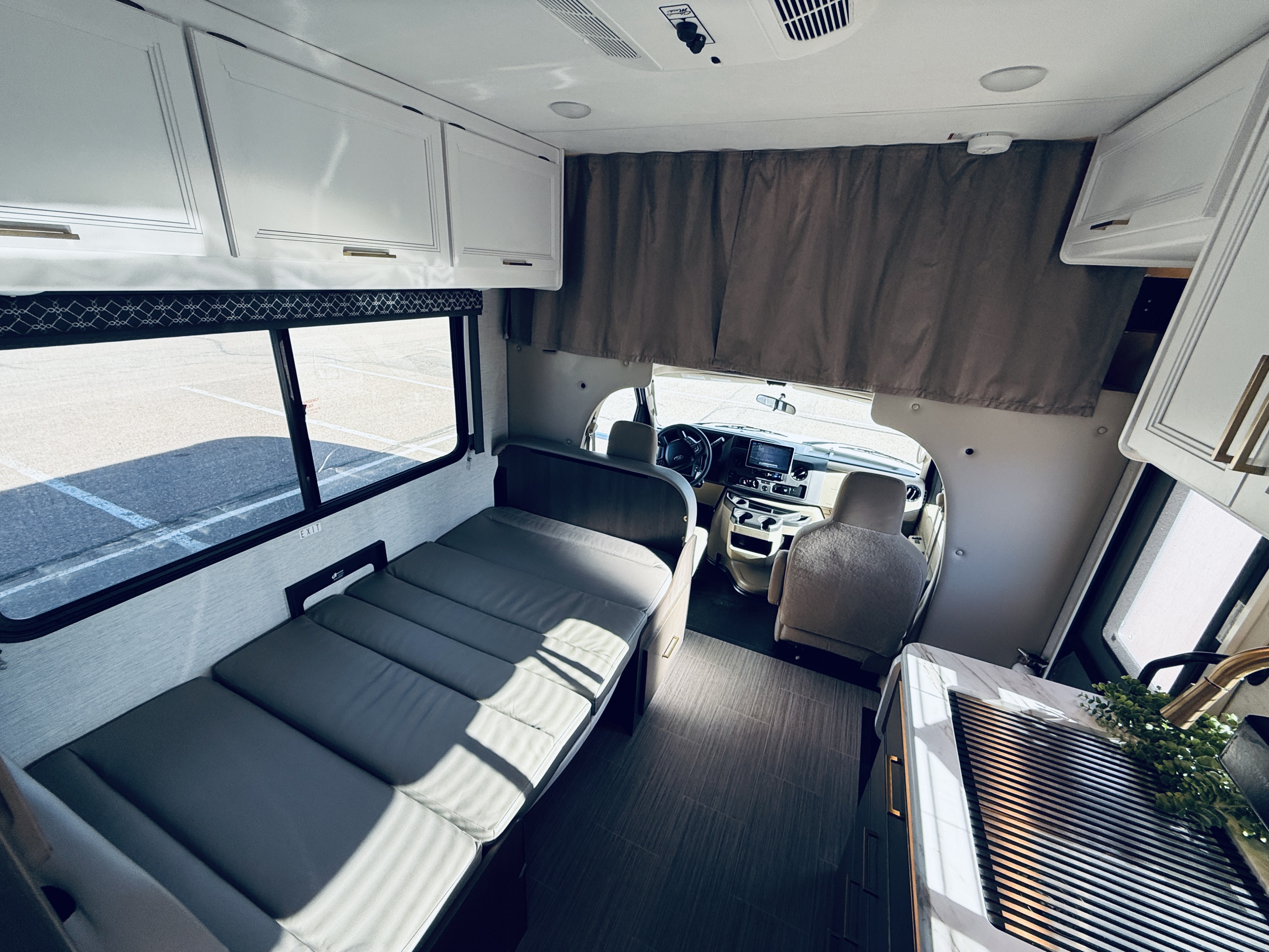 RV rental interior with bed, kitchen, and driver's area, showcasing compact living space on a sunny day.. Thor Freedom Elite 2025