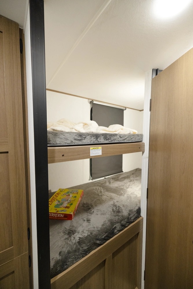 RV rental bunk beds: Top bunk with cozy blanket, lower bunk with Operation game. Ideal compact space for campers.. Coachmen Apex Nano 194BHS 2026