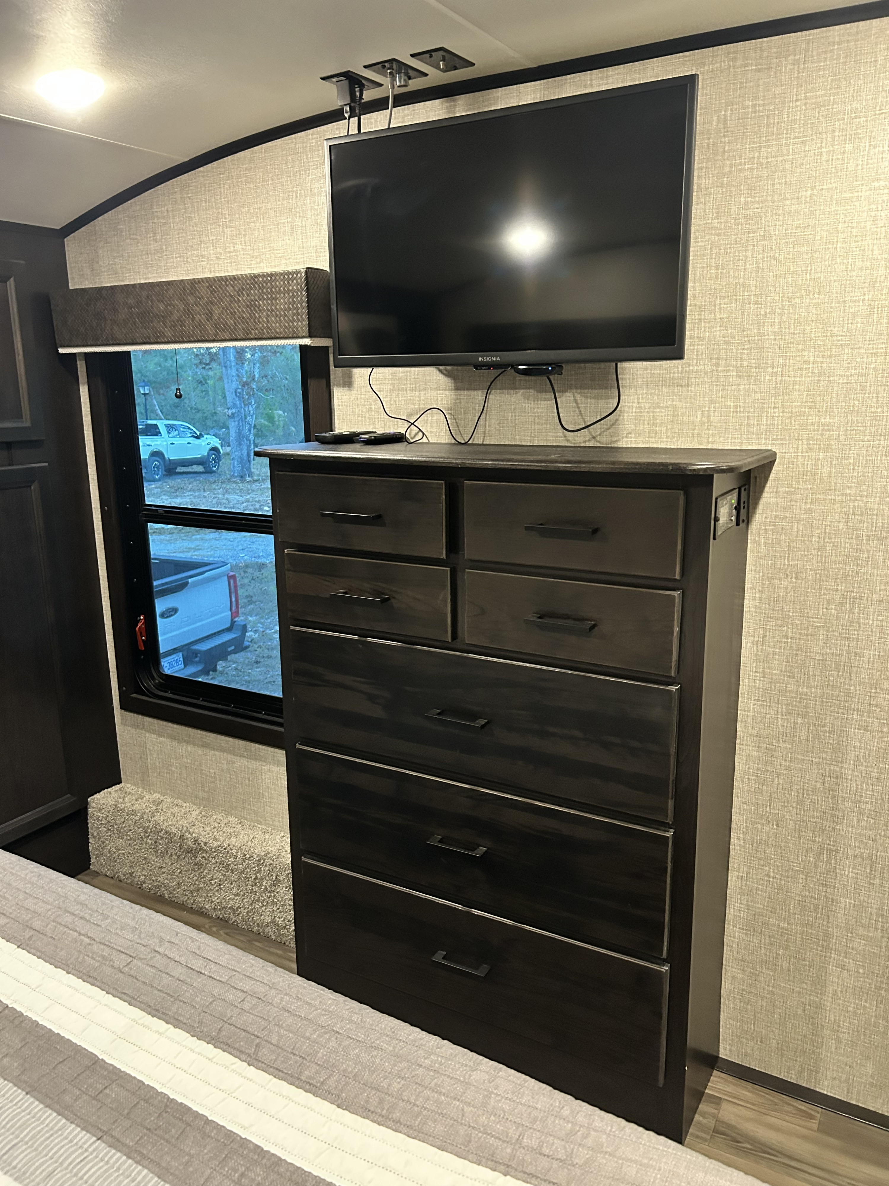 RV rental bedroom: dark dresser with TV mounted above, next to a window view of outside, with a bed visible.. Jayco Eagle 2022