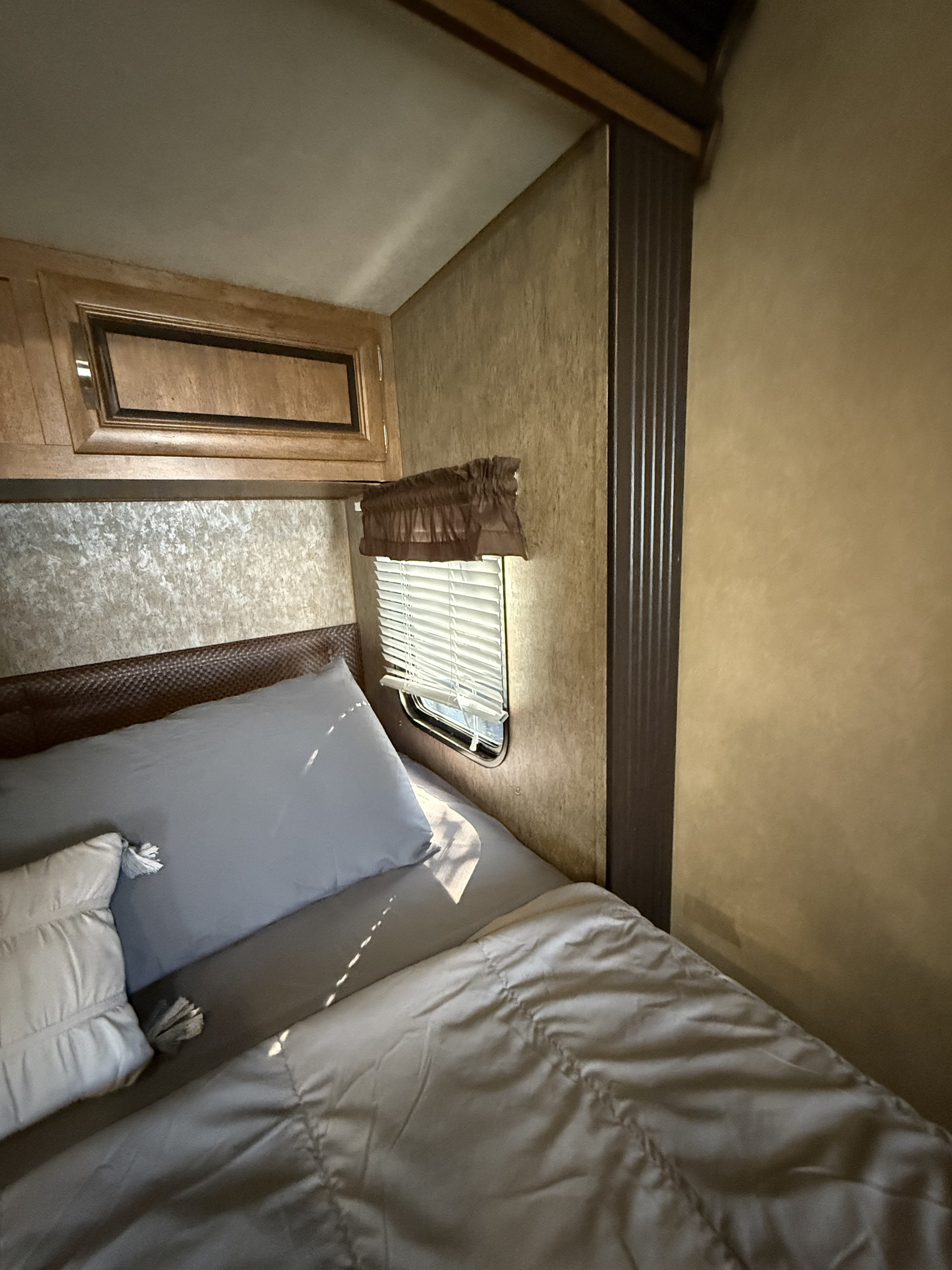 A warm, sunlit bedroom inside an RV rental, showing a bed with blue and white pillows, a window, and wood cabinets.. Salem 36BHBS 2017