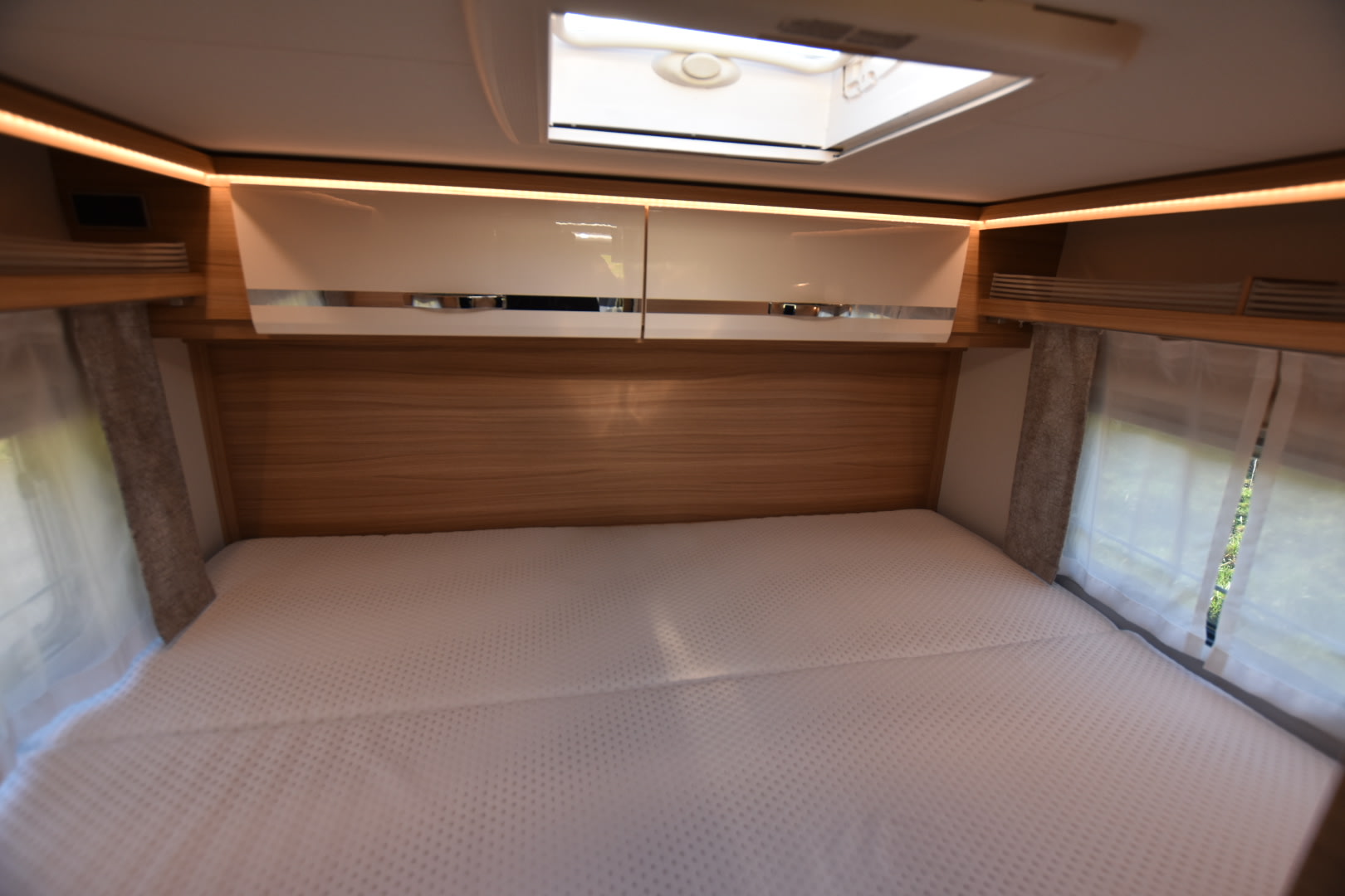 Cozy RV rental bedroom with white mattress, overhead cabinets, and ambient lighting, perfect for a comfortable night's sleep.. Dethleffs Globebus I 1 2021